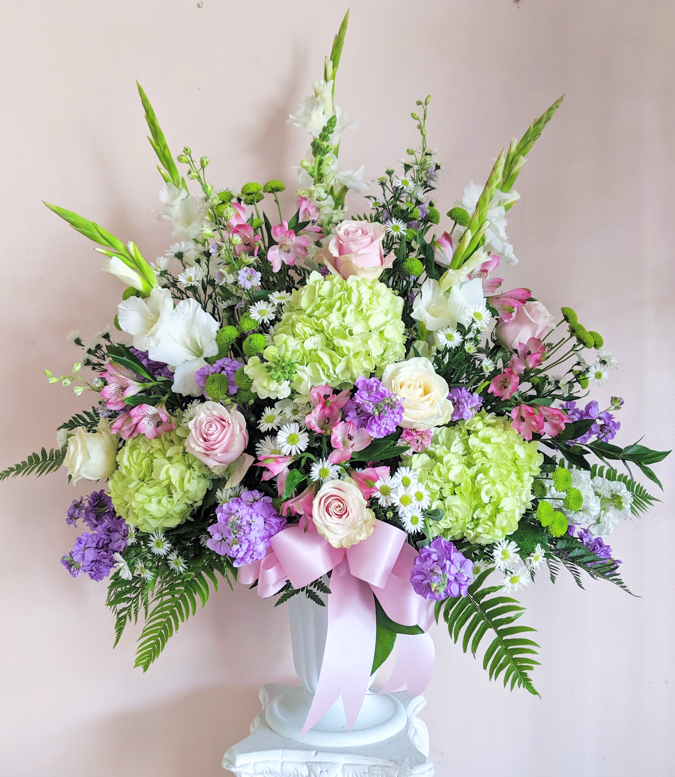 Large pastel floral arrangement in a white vase with a pink ribbon