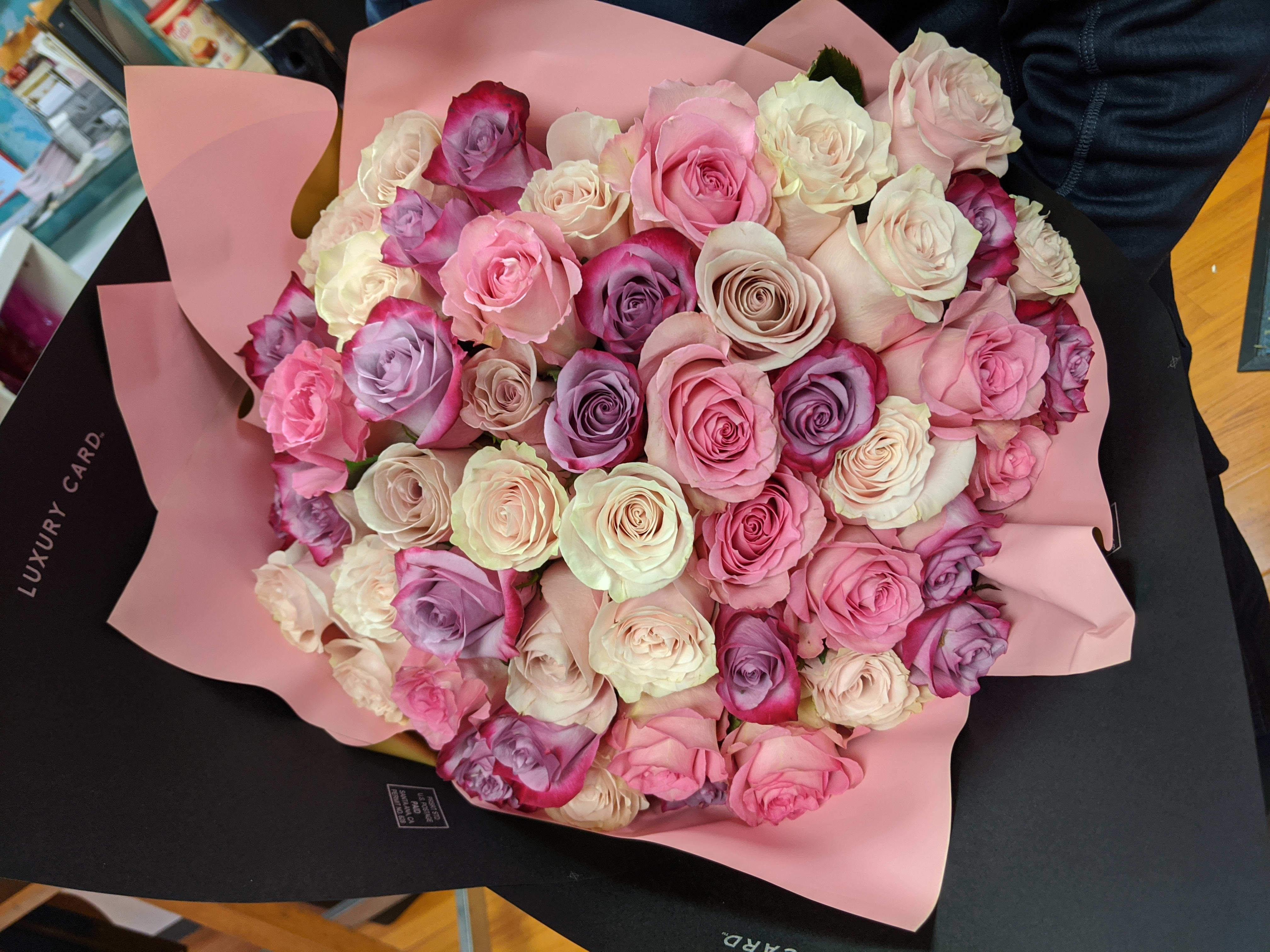 Large bouquet of pink, white, and lavender roses wrapped in pink paper
