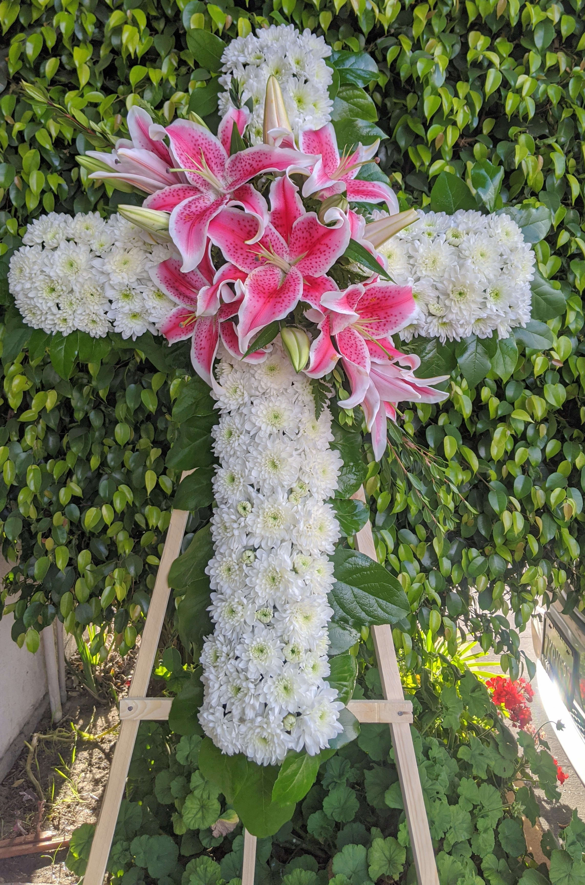 Pink lilies and white chrysanthemums arranged in a cross on a stand