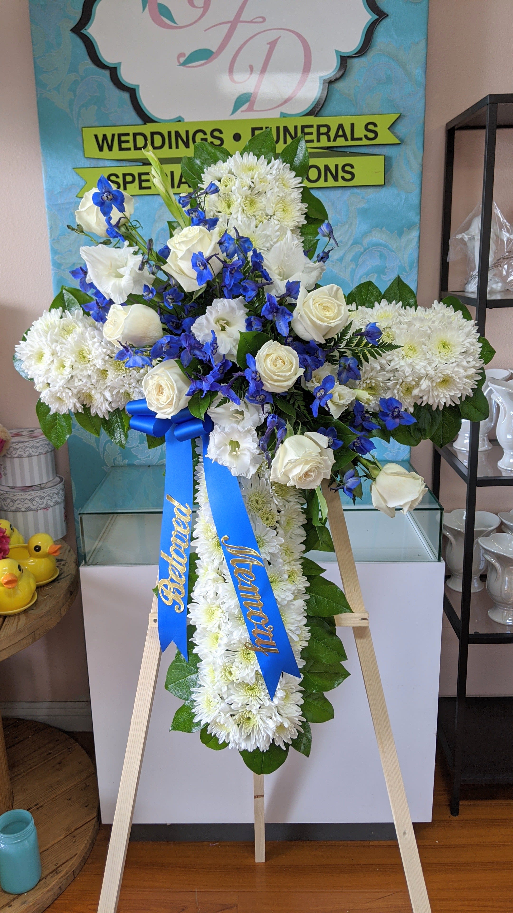 White and blue funeral standing spray on an easel with ribbon streamers
