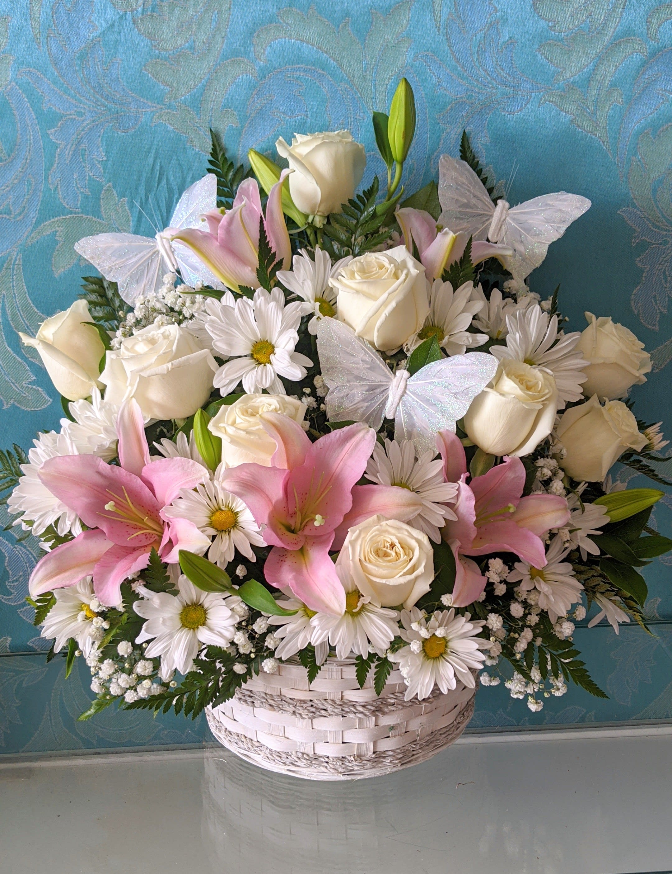 Basket arrangement of white roses, pink lilies, and daisies with butterfly accents