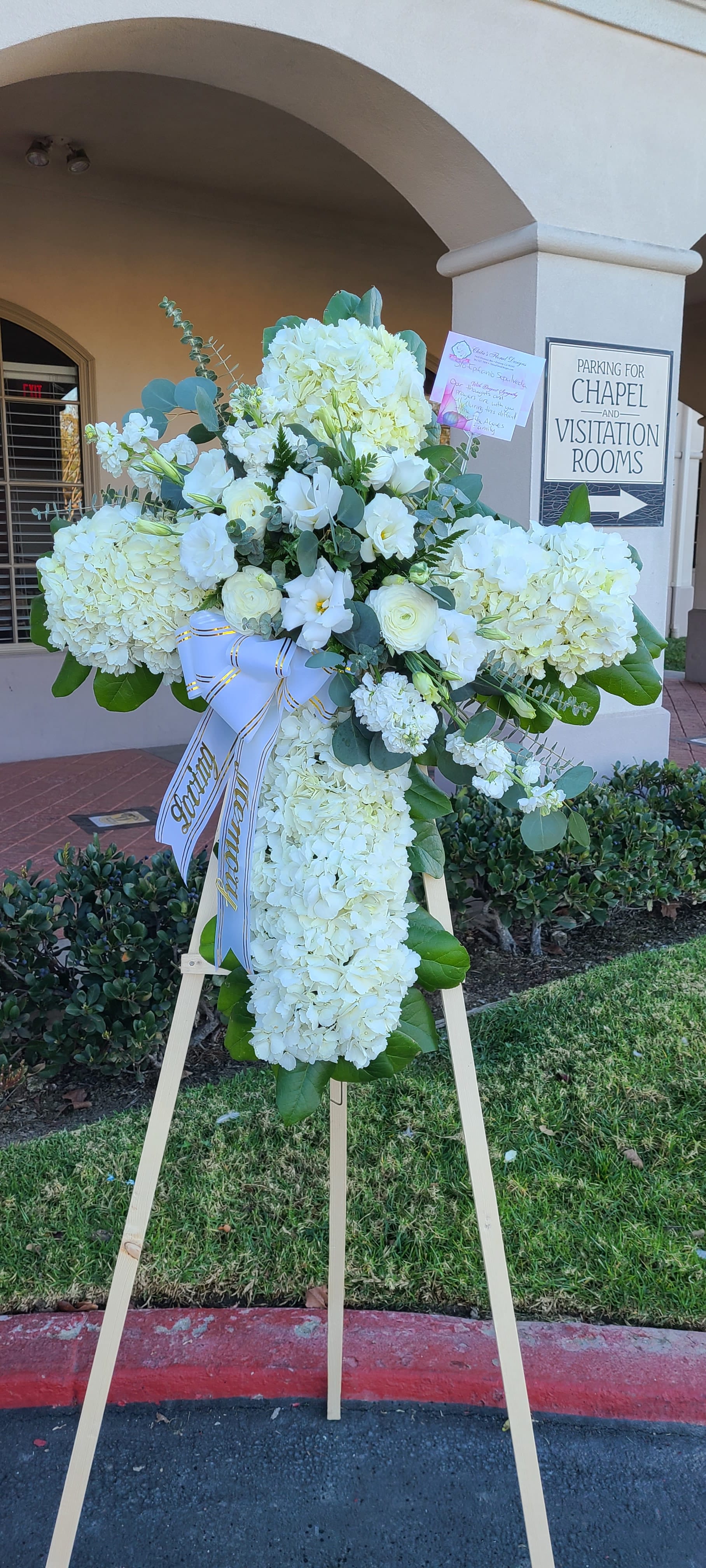 White funeral standing spray on an easel with a ribbon