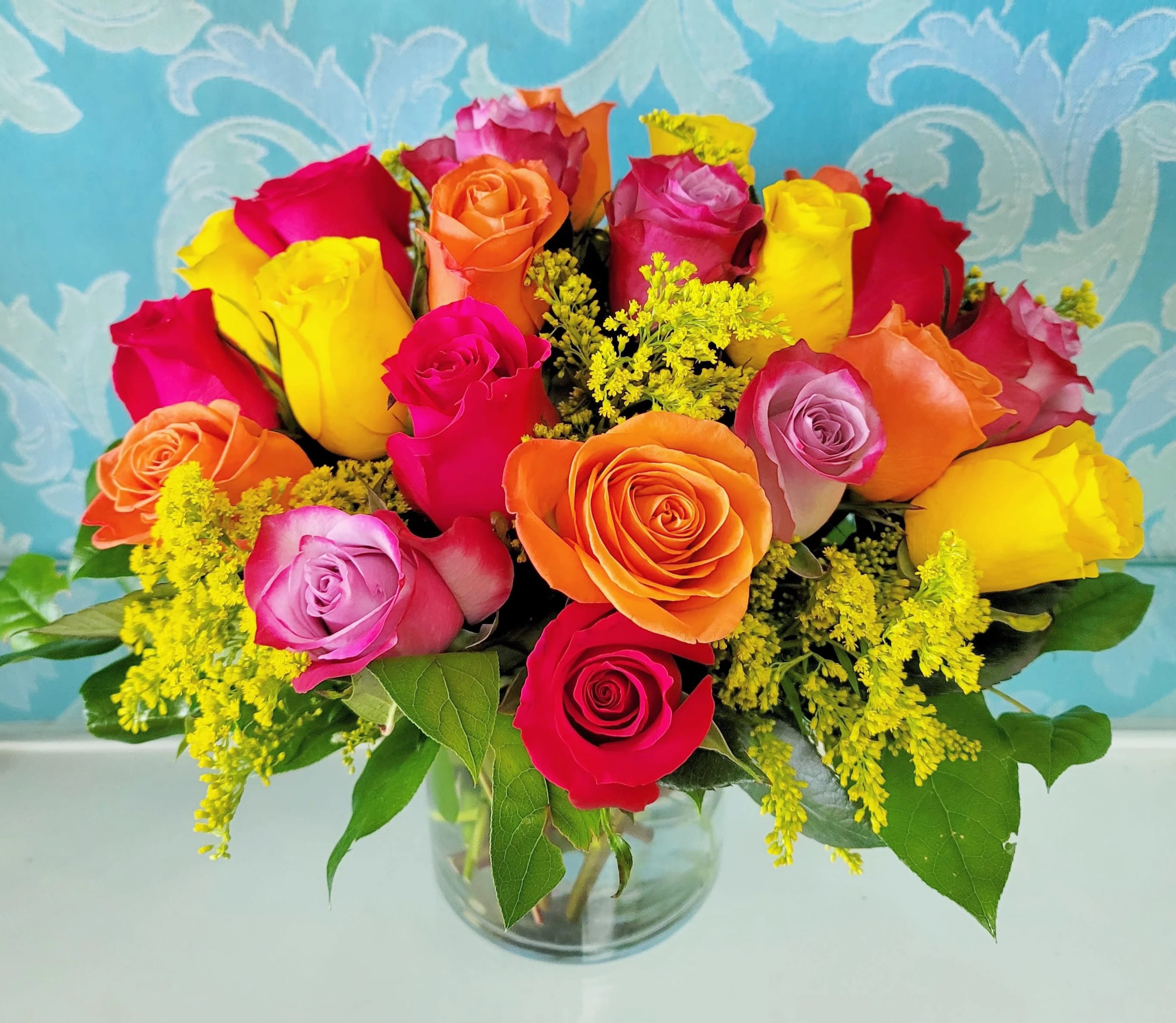 Vibrant bouquet of multicolored roses with yellow filler flowers in a clear glass vase