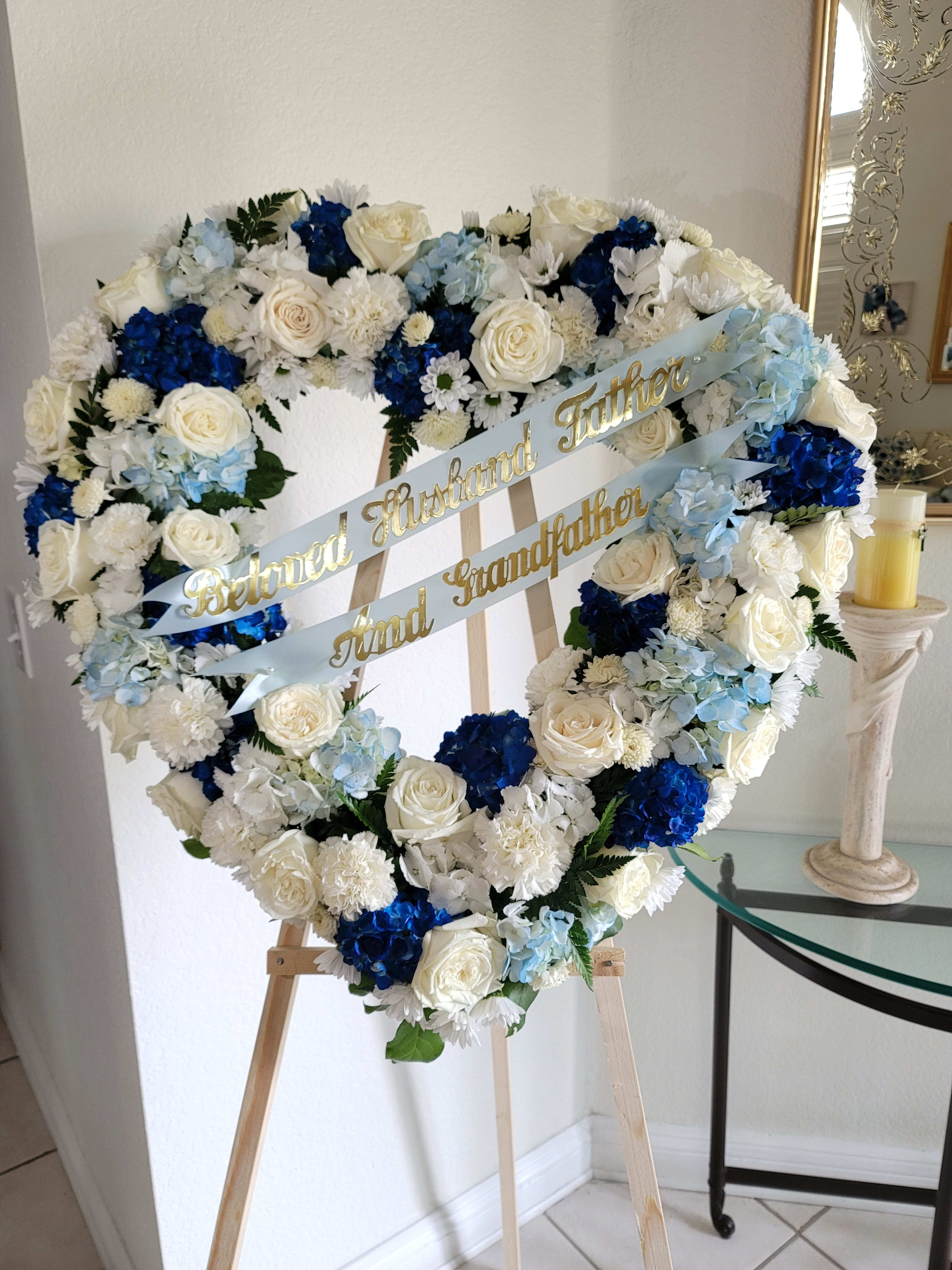 Heart-shaped floral wreath with white, blue, and pale blue flowers on an easel