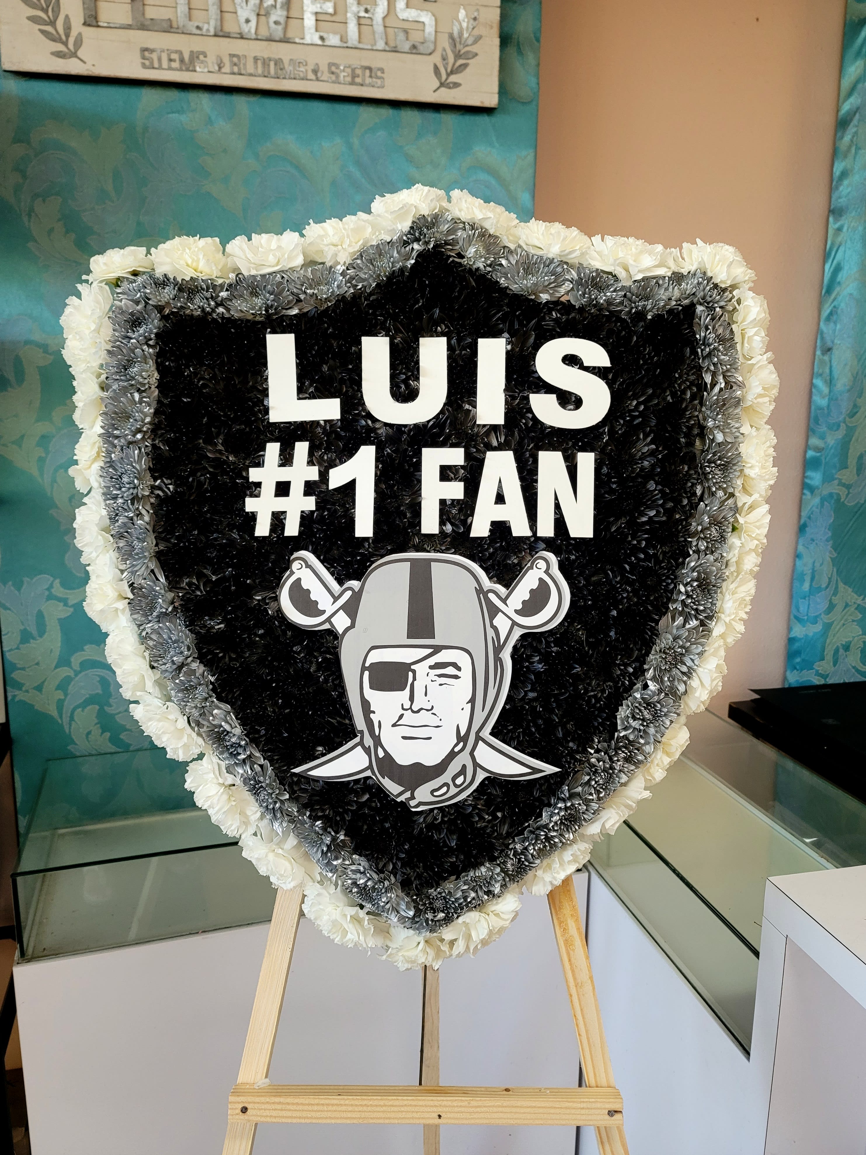 Heart-shaped floral tribute with black, white, and silver flowers and a sports logo