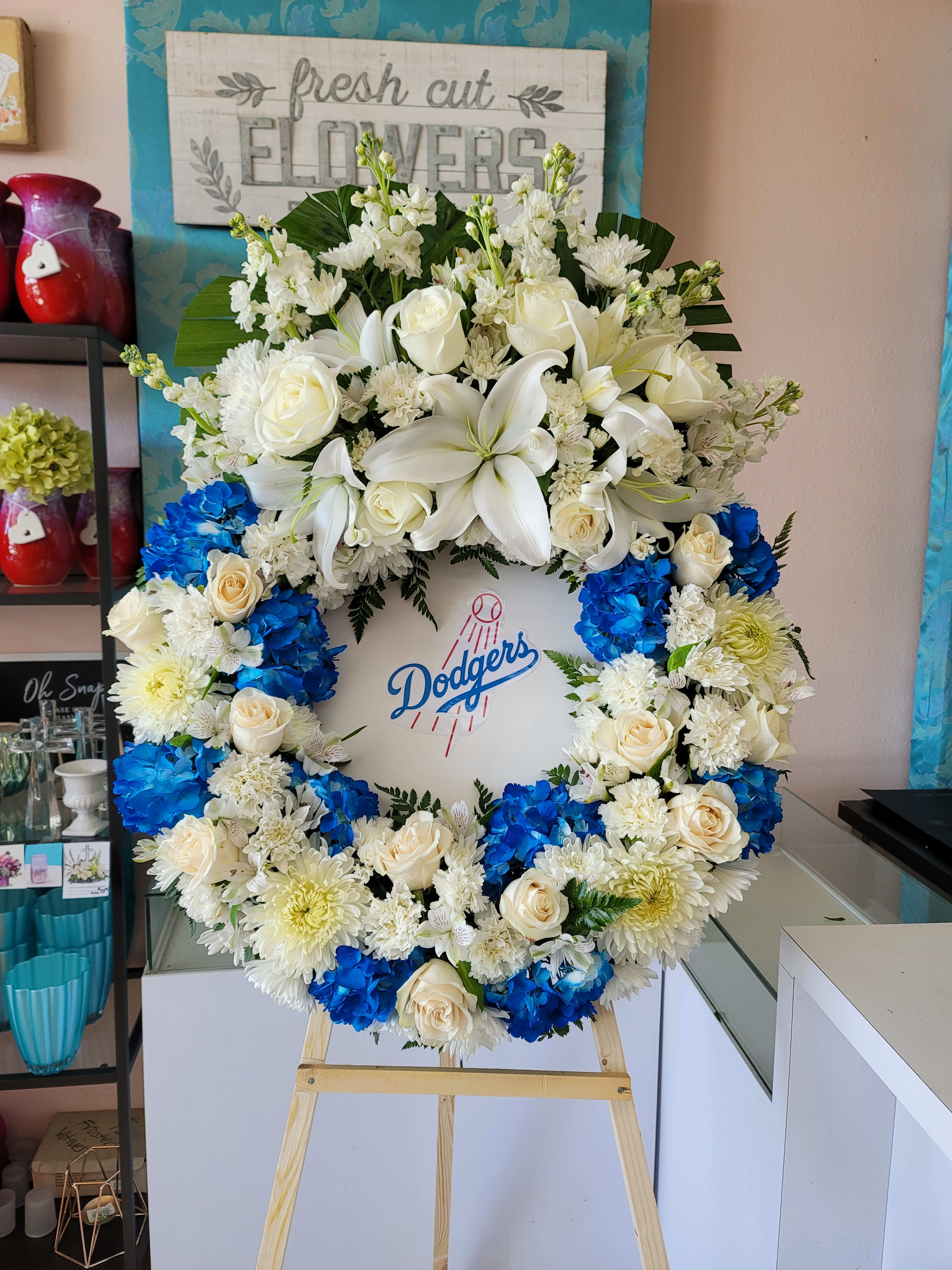 Large floral wreath with white lilies, roses, and blue hydrangeas around a Dodgers logo