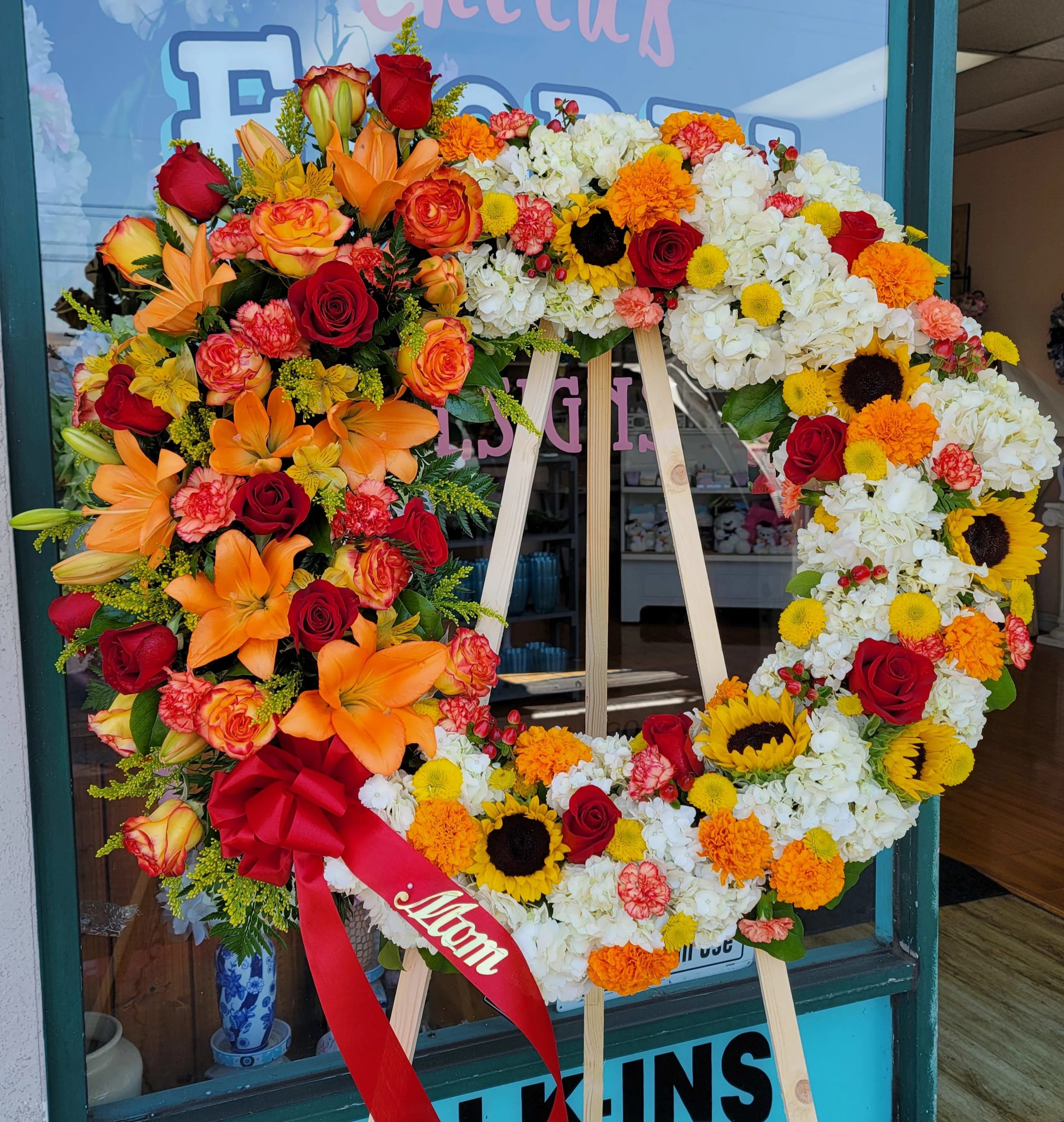 Large floral wreath on an easel with red, orange, yellow, and white flowers