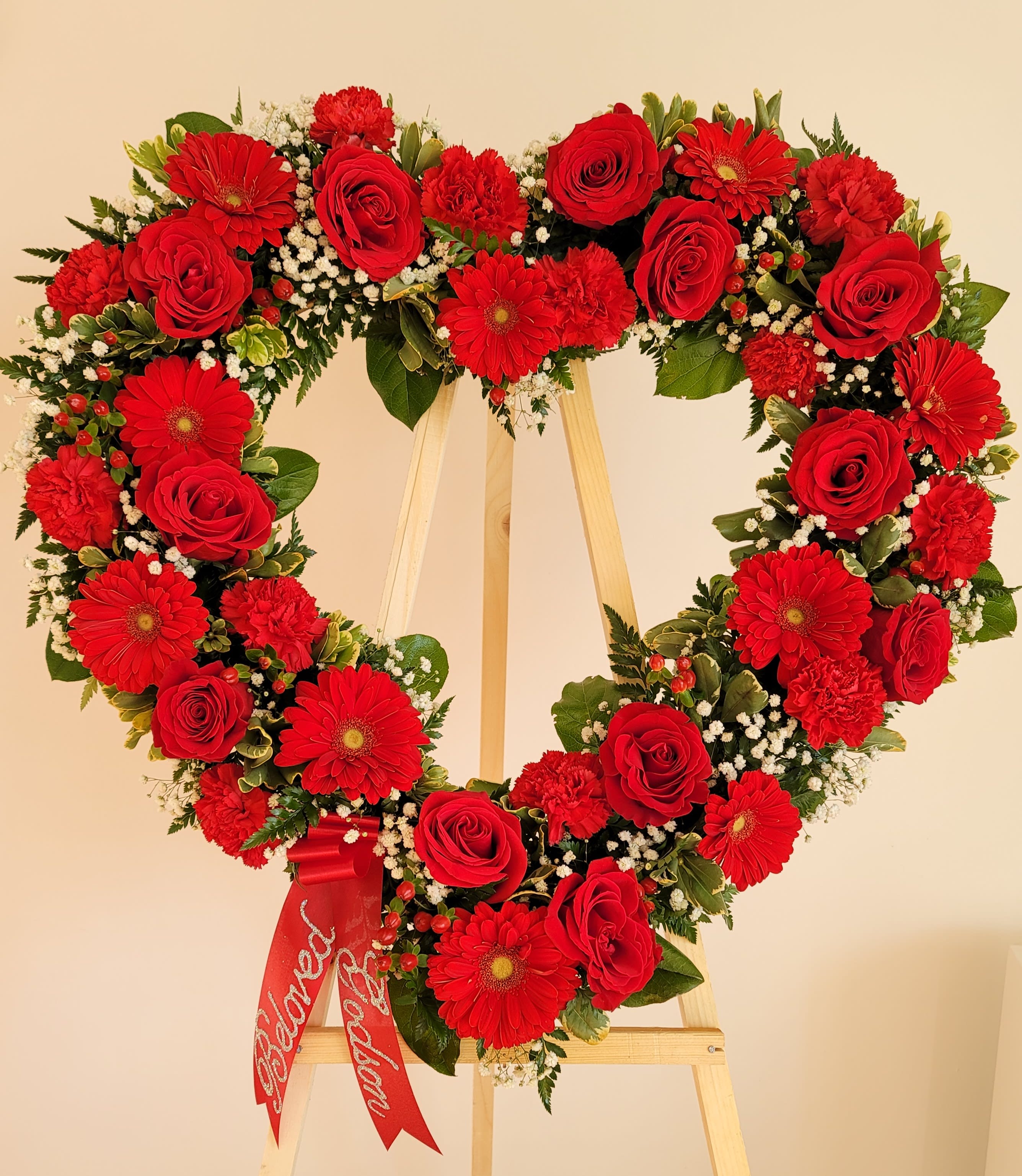 Heart-shaped floral wreath with red roses and gerbera daisies on an easel