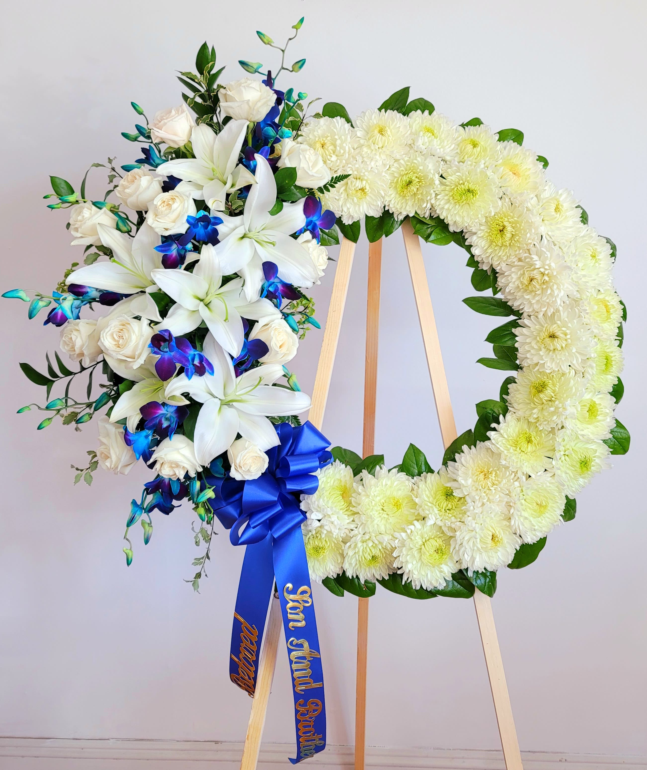 White floral funeral wreath on an easel with blue ribbon