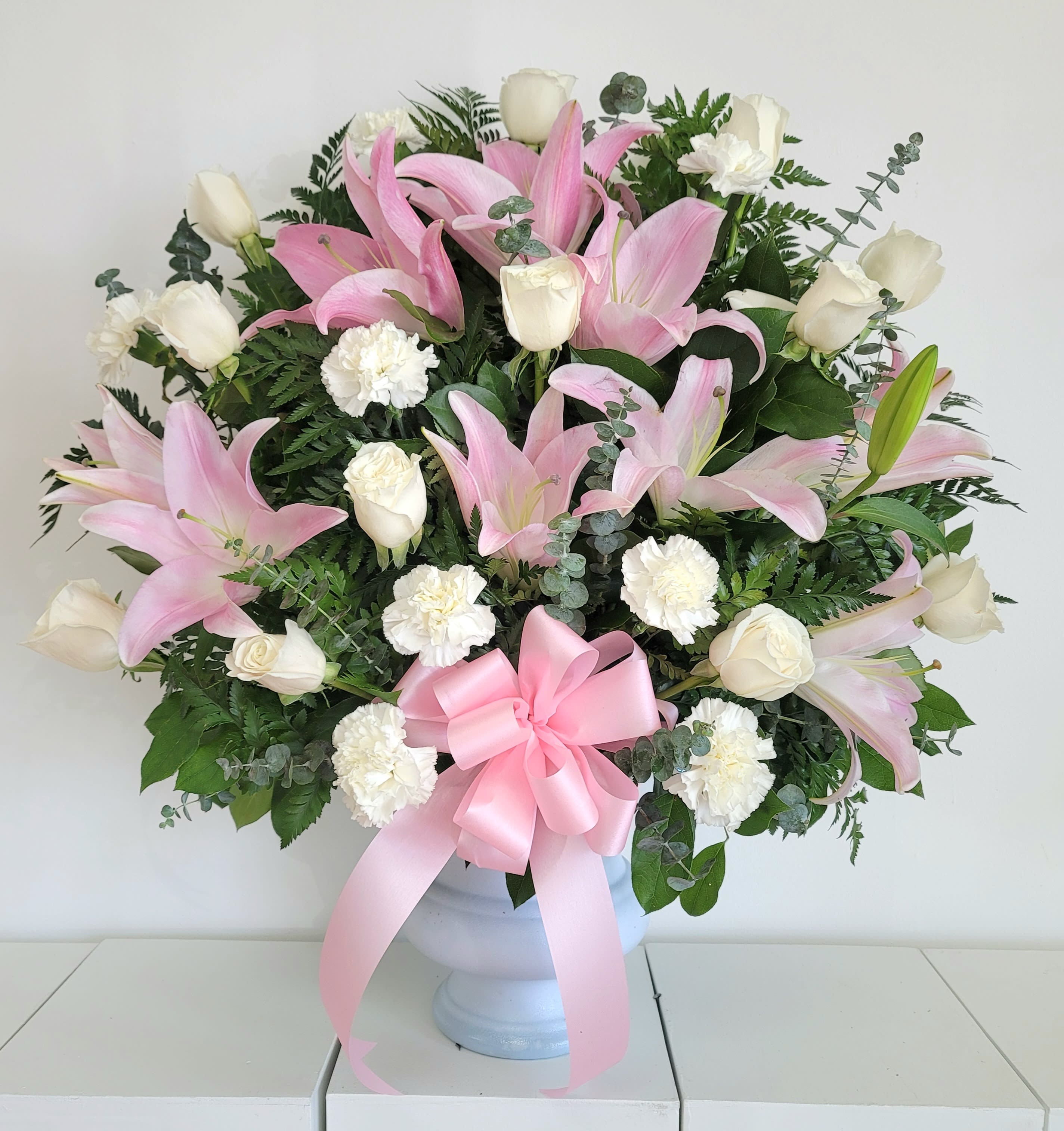 Pink lilies and white roses in a white vase with a pink ribbon