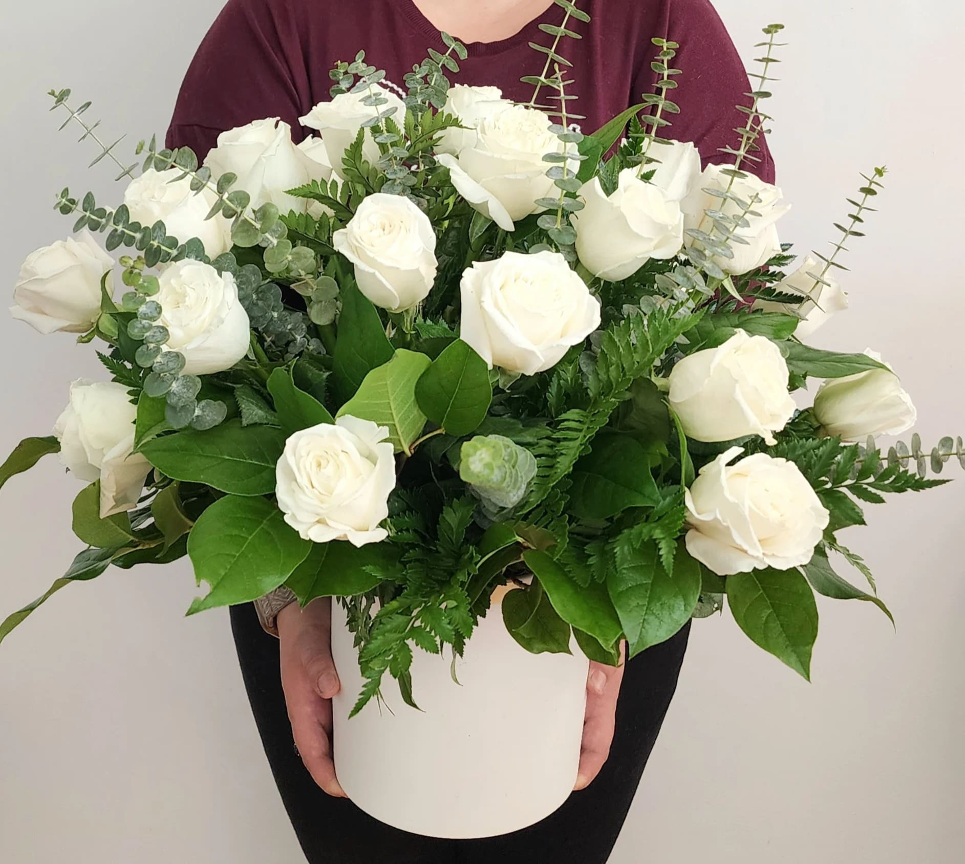 White roses in a white hatbox with eucalyptus and greenery