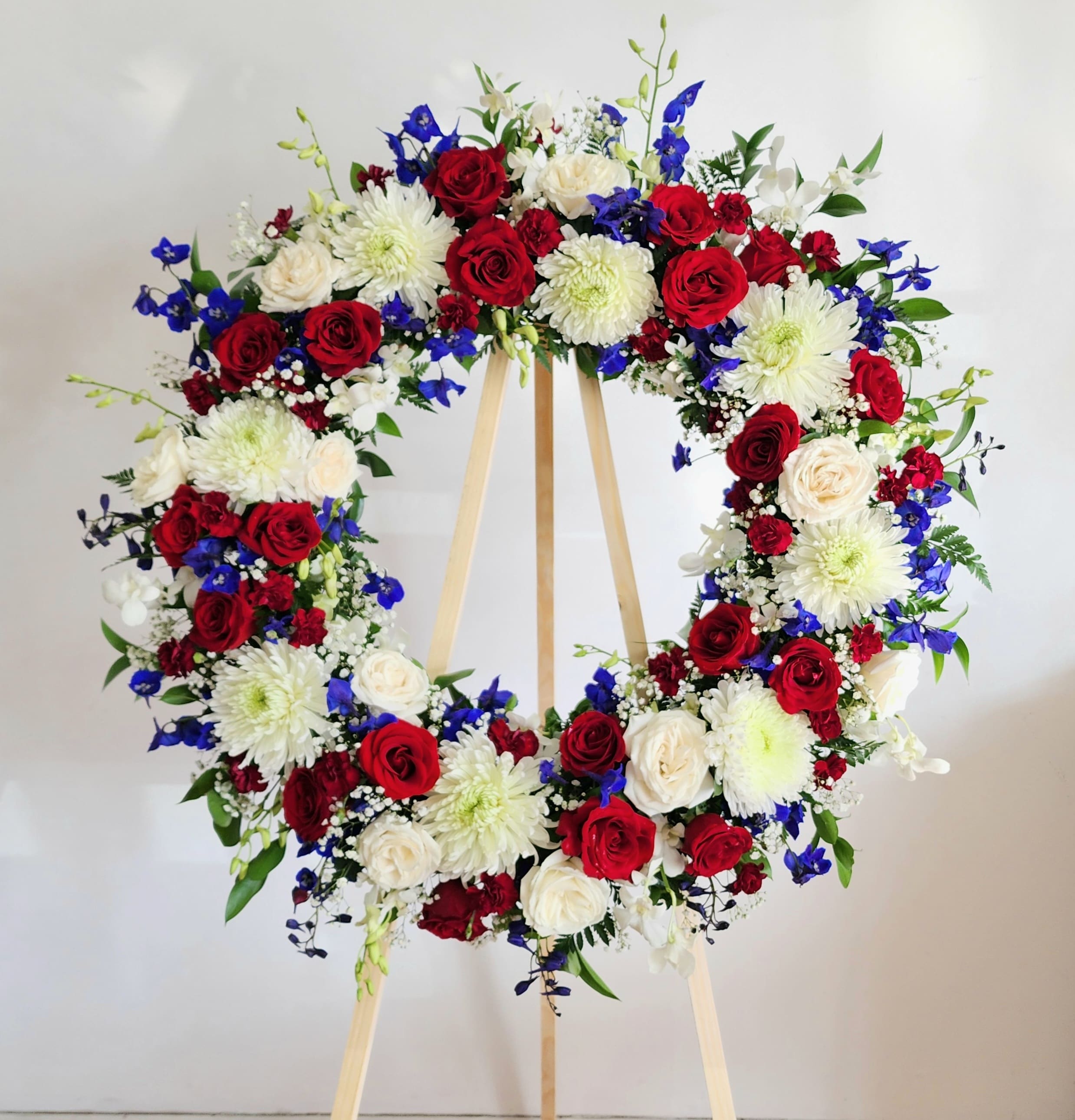 Heart-shaped floral wreath with red, white, and blue flowers on a wooden stand