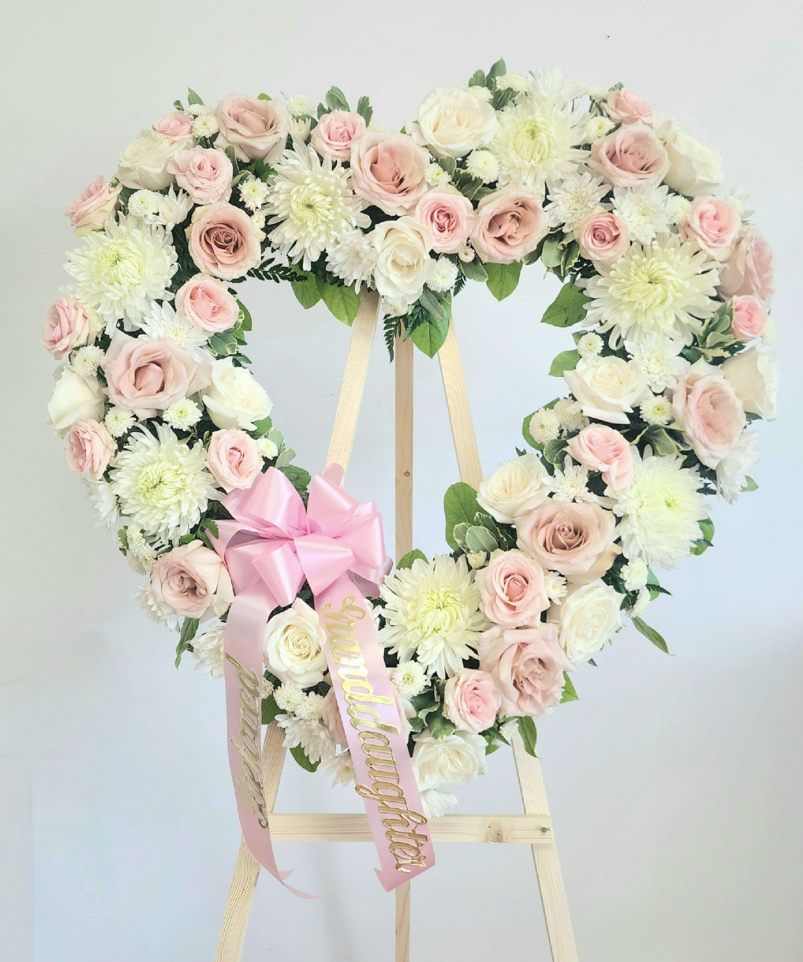 Heart-shaped floral wreath of pink and white roses on a wooden easel