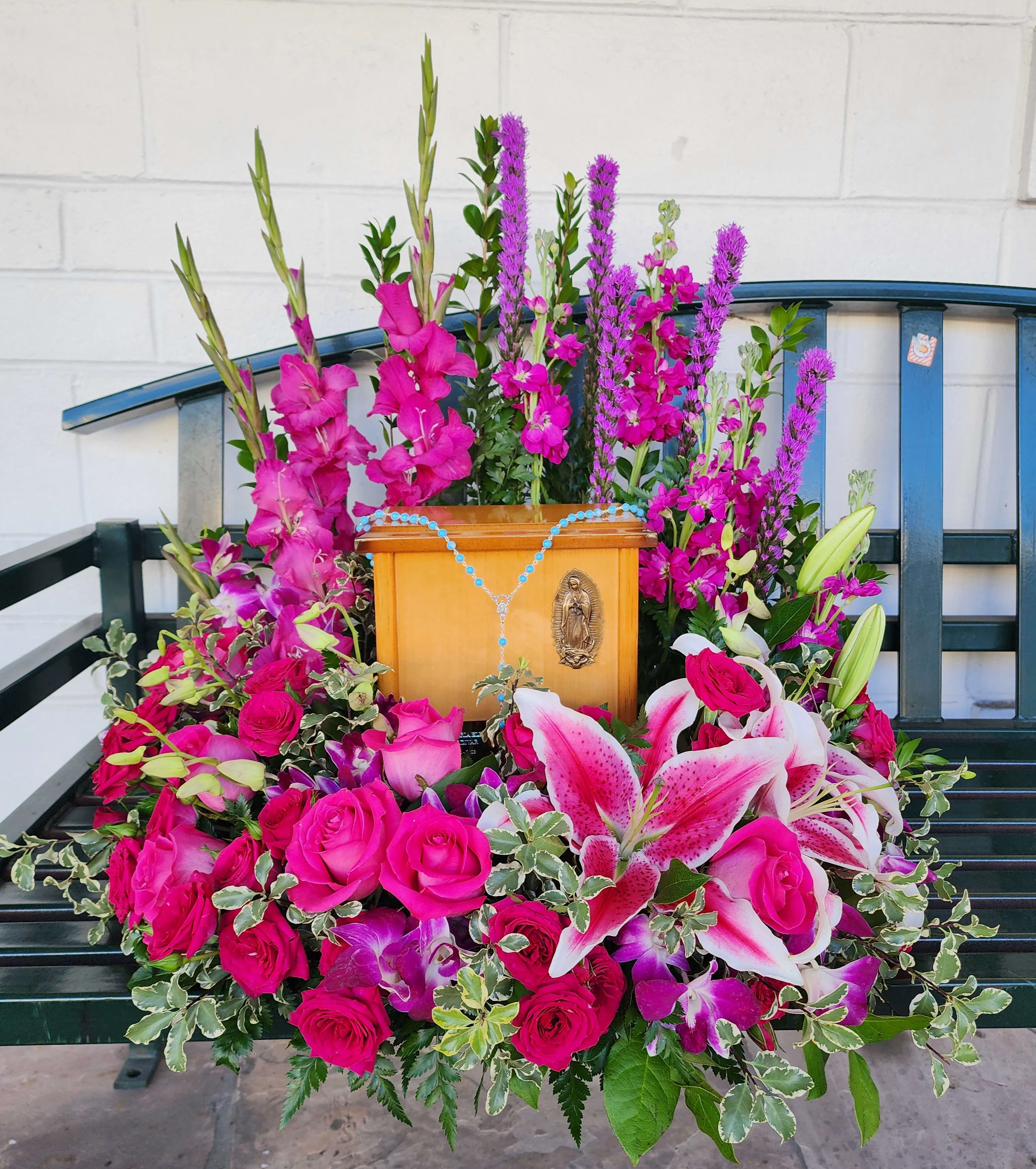 Pink floral arrangement around a wooden religious plaque on a bench