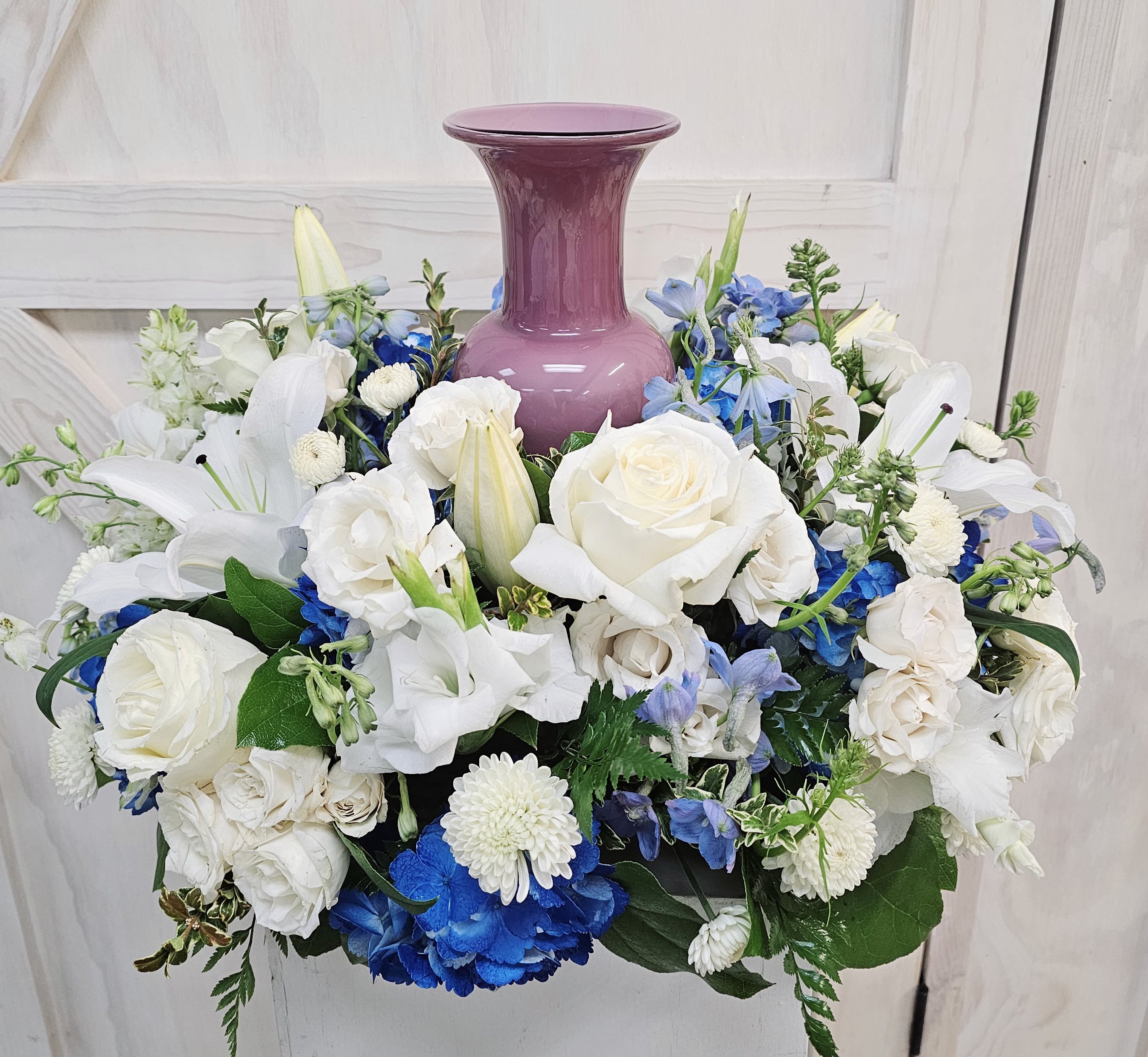 White and blue floral arrangement around a purple vase