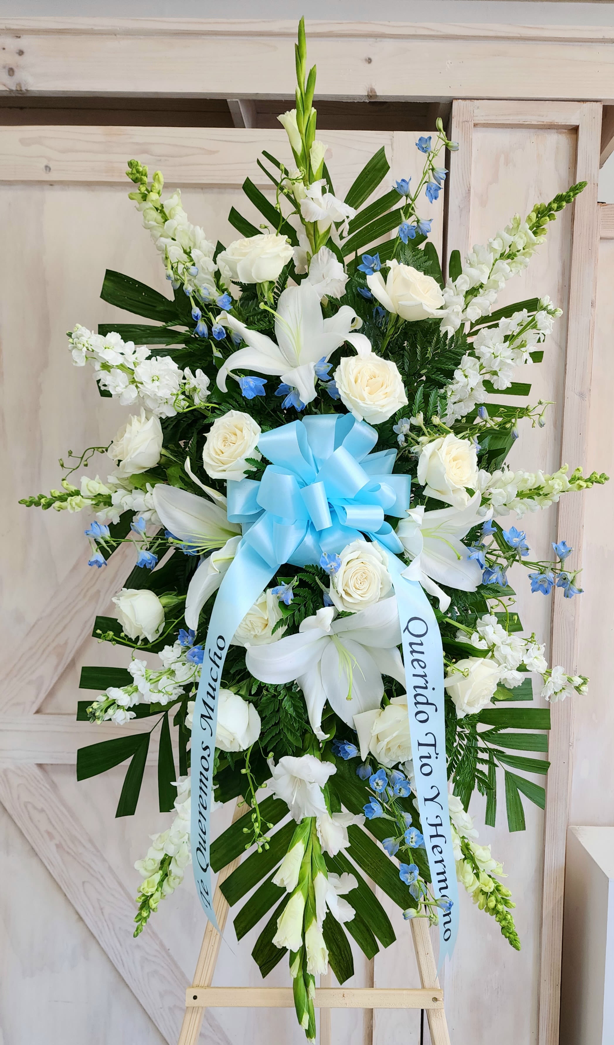 Standing funeral spray of white lilies and roses with blue accents and a ribbon