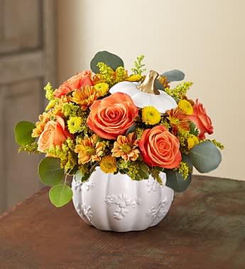 Orange and yellow floral arrangement in a white pumpkin vase
