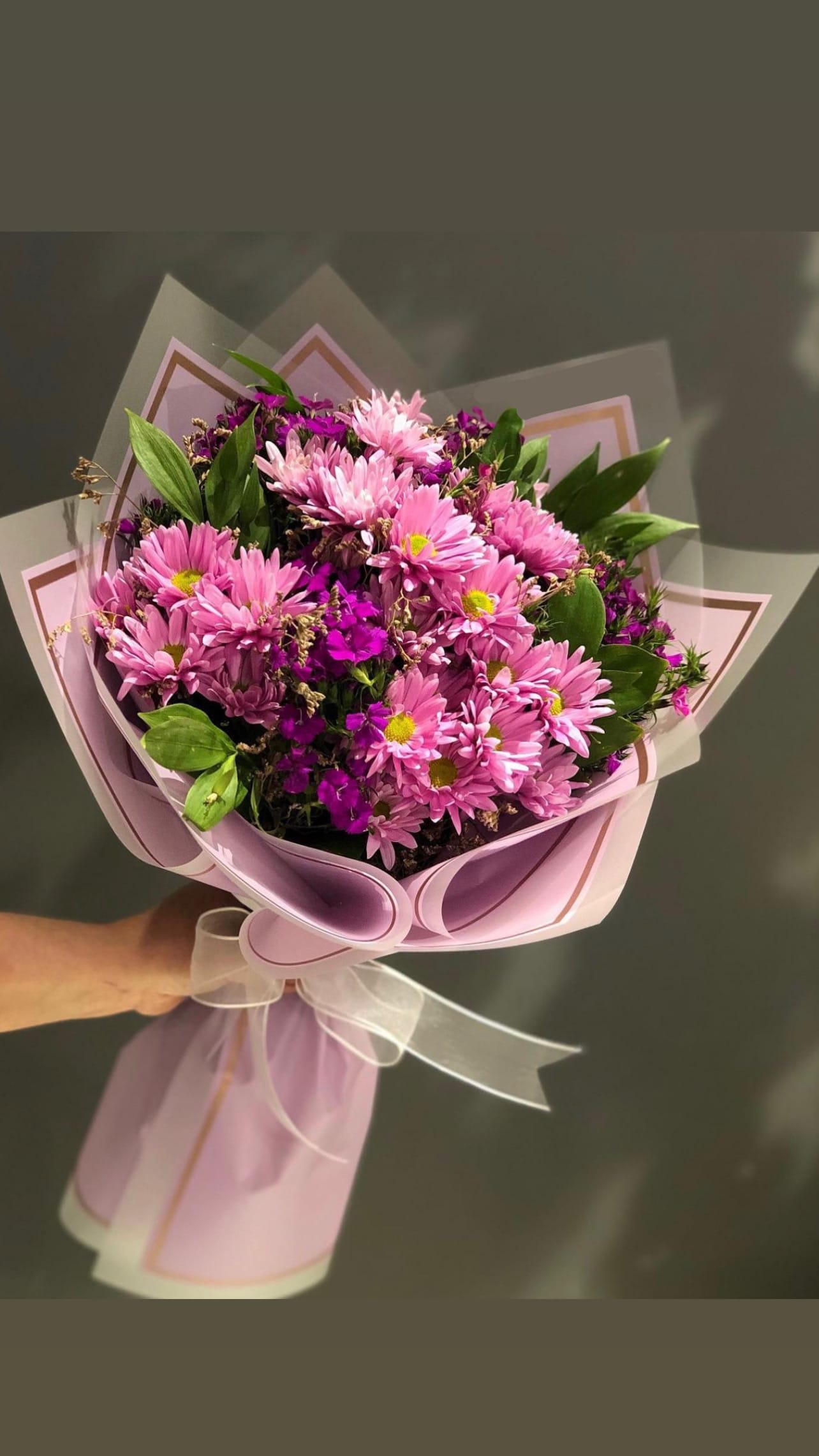 Pink daisy bouquet wrapped in pastel paper with a white ribbon