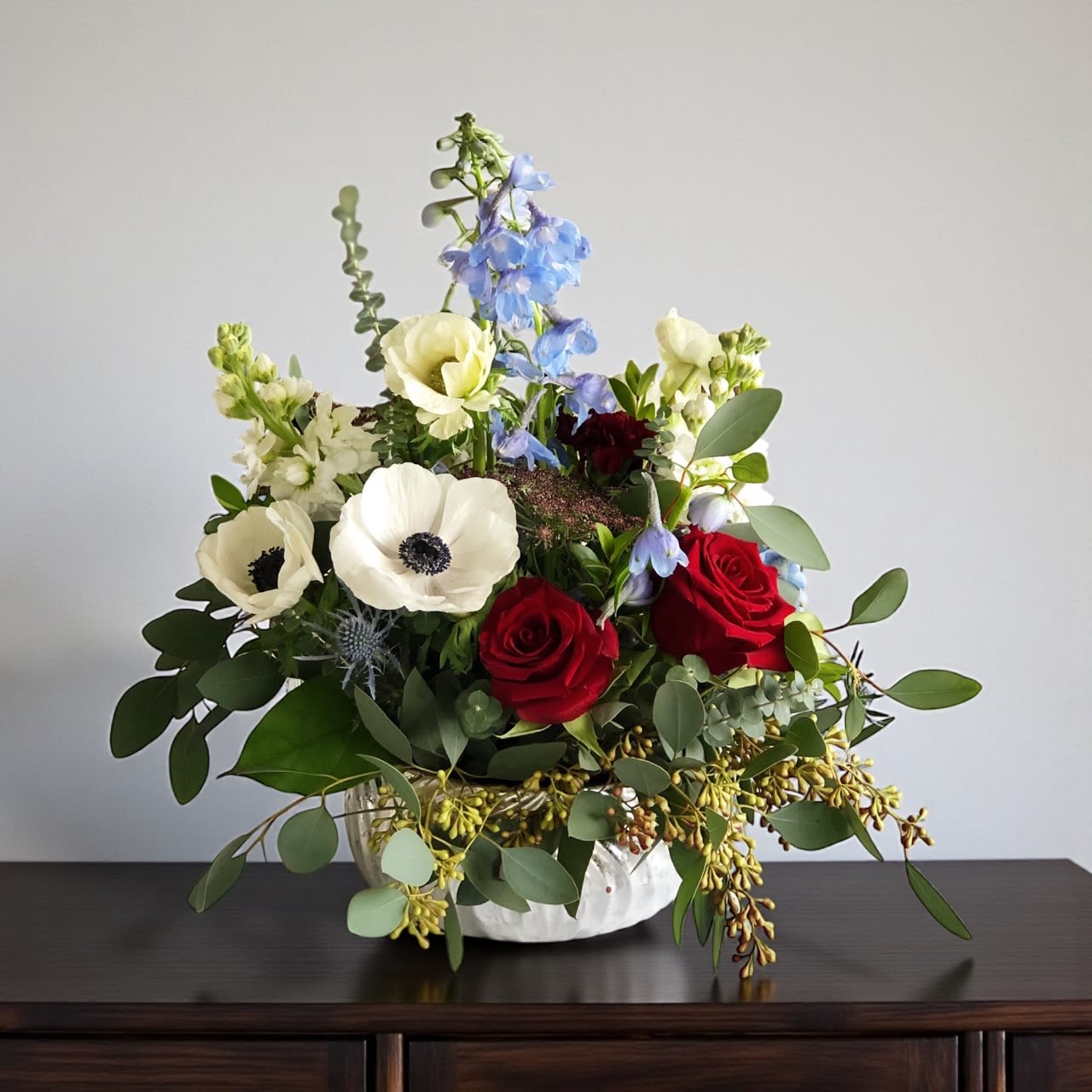 Mixed bouquet in a white vase with red roses, white anemones, and blue delphinium