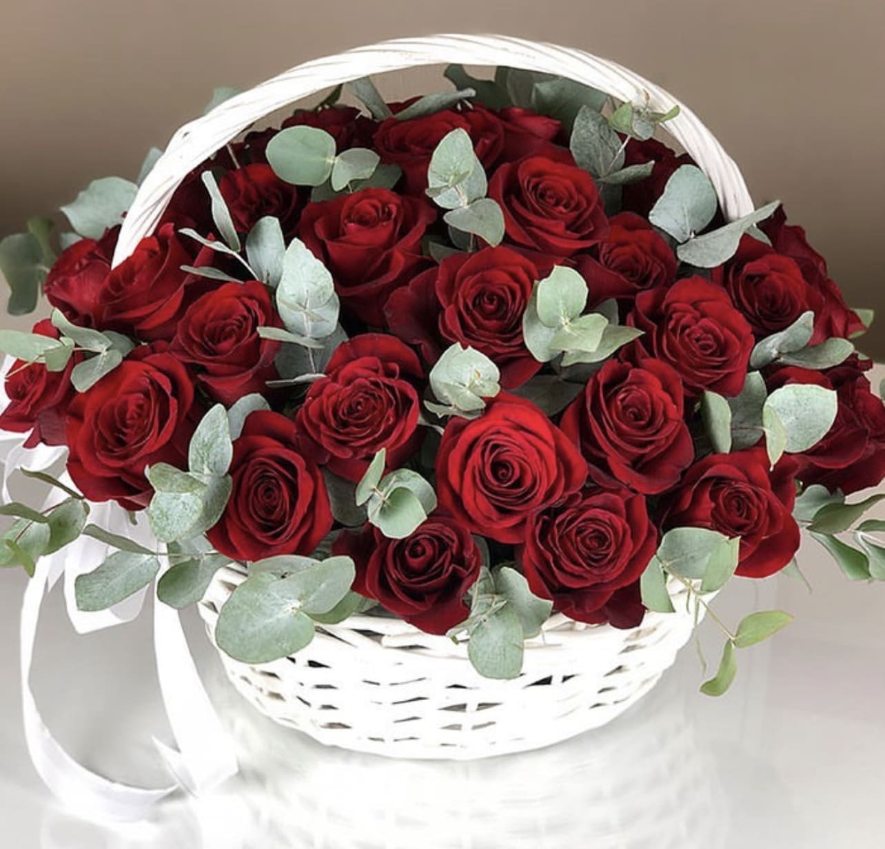 Basket of red roses with eucalyptus and a white ribbon handle