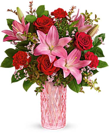 Pink lilies and red roses arranged in a pink glass vase