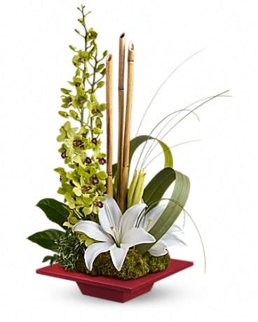 White lilies in a red square vase with tall green stems and bamboo accents