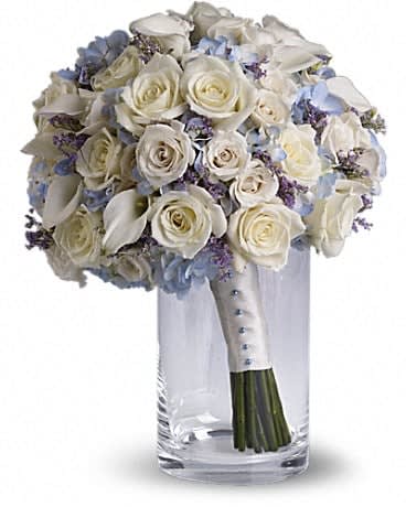 White rose bouquet with pale blue flowers in a clear glass vase