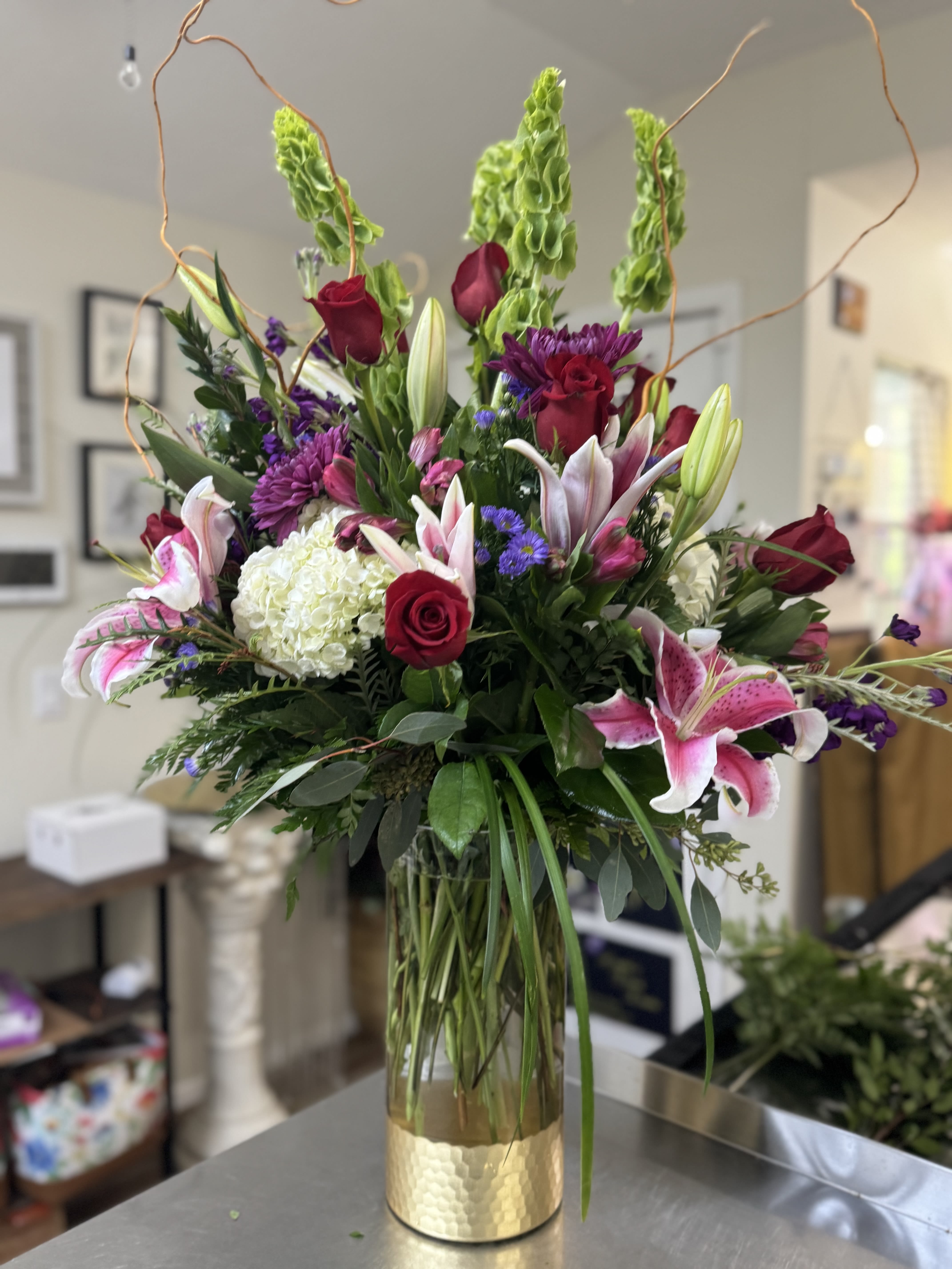 Tall mixed bouquet in a glass vase with red roses, lilies, and purple flowers