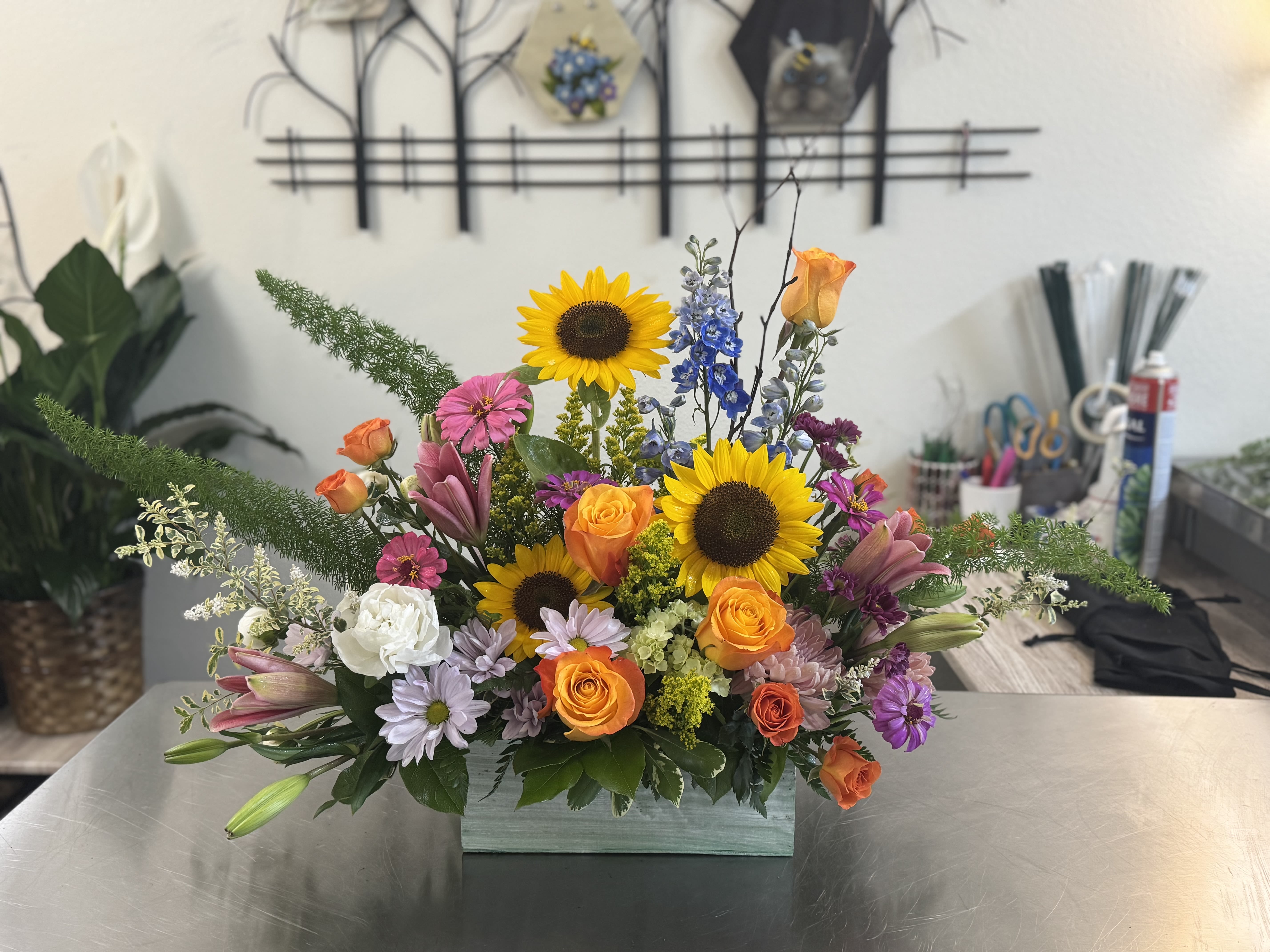 Mixed bouquet with sunflowers, roses, lilies, and daisies in a rectangular vase