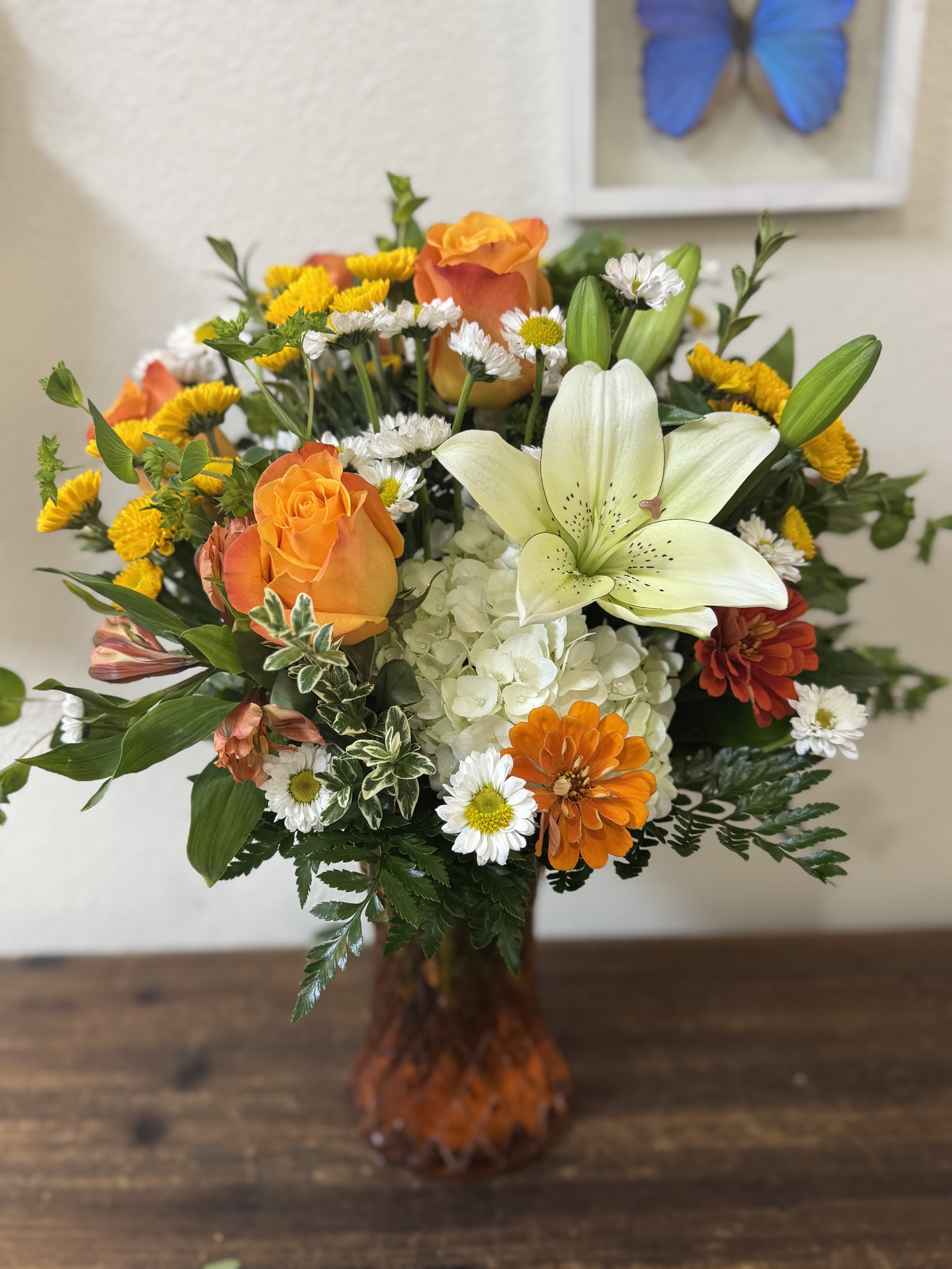 Orange roses and white lilies in a glass vase with mixed daisies