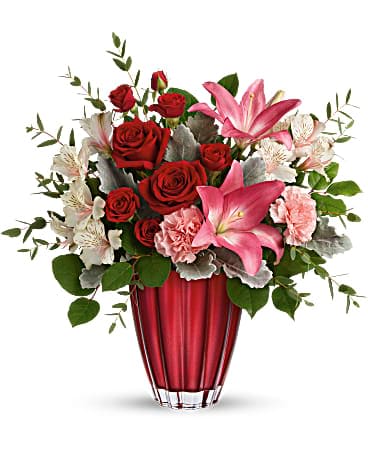 Red roses and pink lilies arranged in a red glass vase