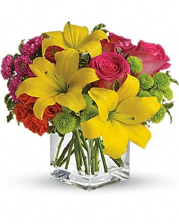 Bouquet of yellow lilies, pink roses, and green pompons in a clear glass vase