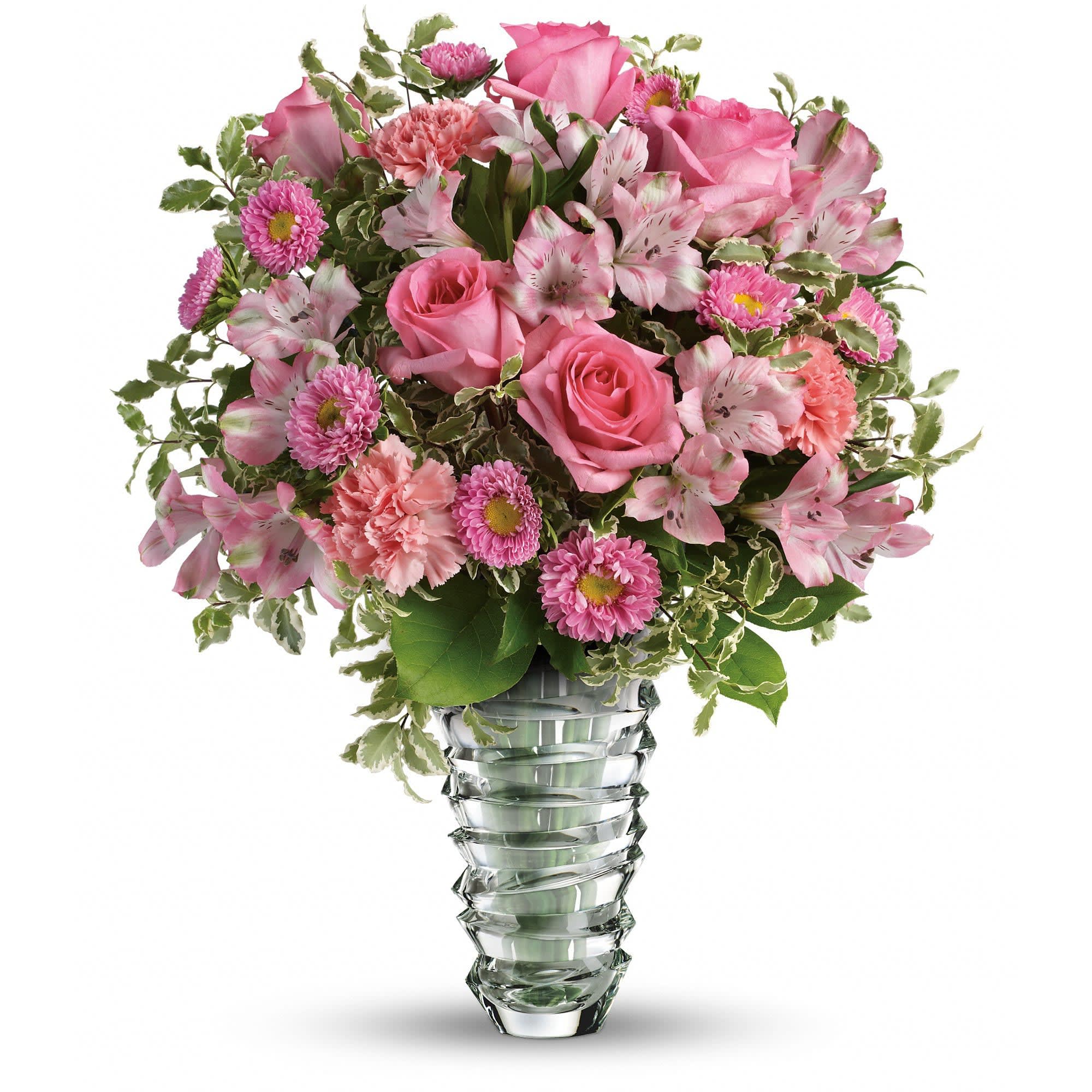 Pink roses, carnations, alstroemeria, and small button flowers in a clear sculpted glass vase with variegated foliage.