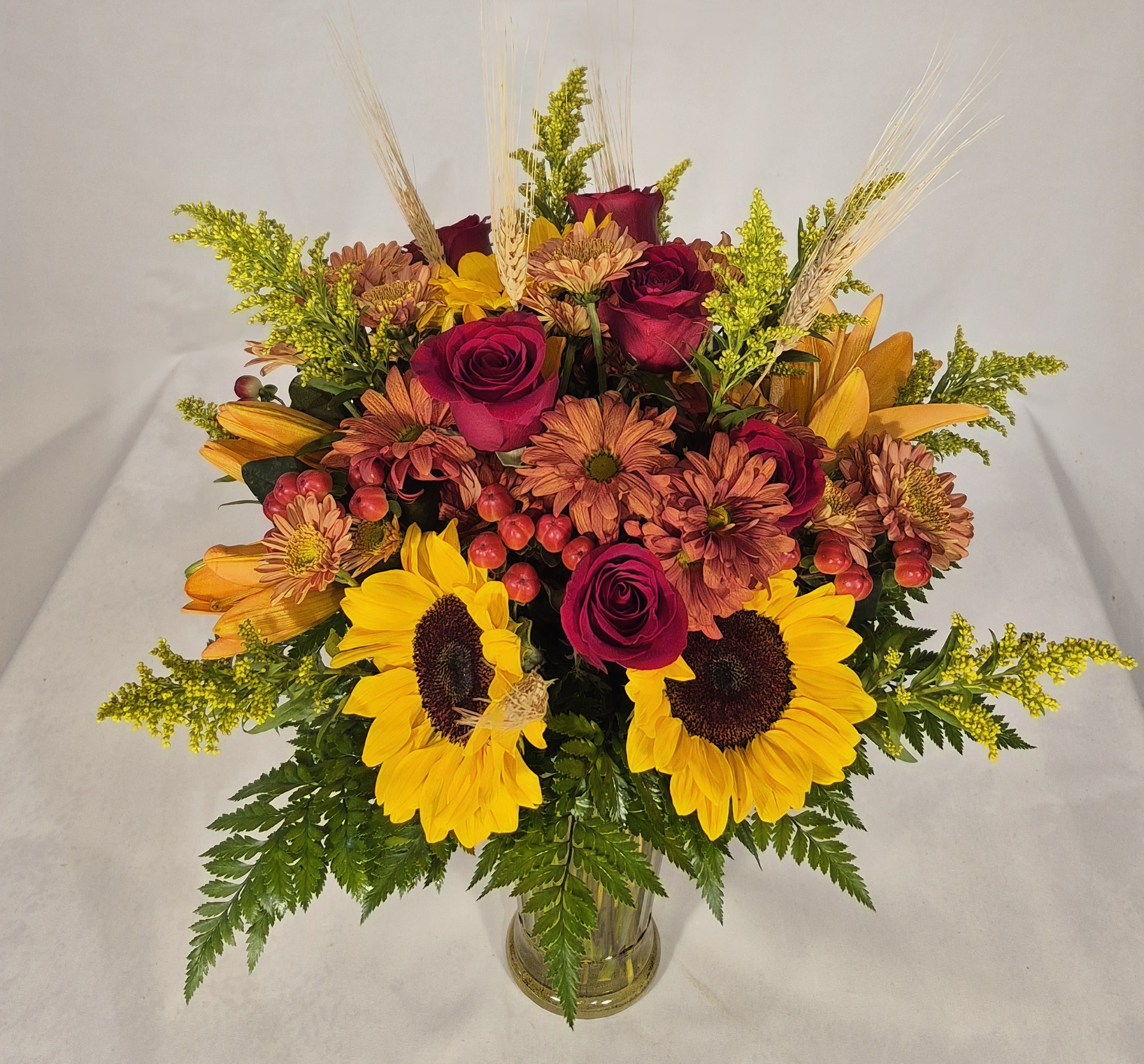 Bouquet of sunflowers, roses, and mums in a clear glass vase