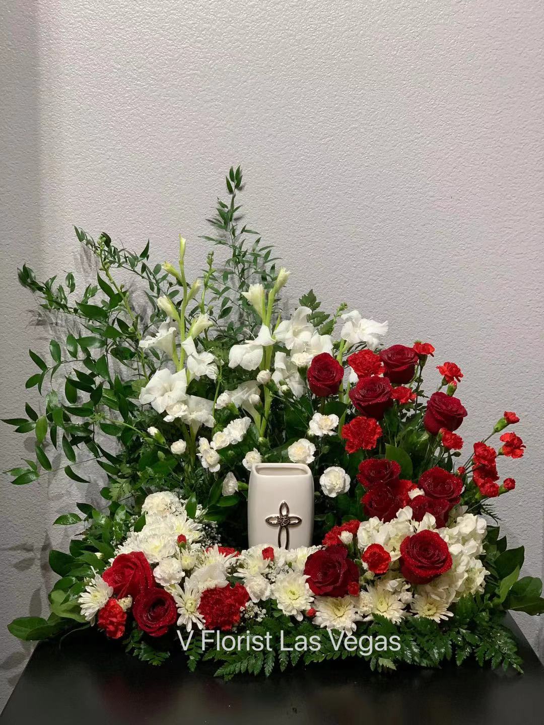 Red and white floral arrangement with a white urn and cross centerpiece