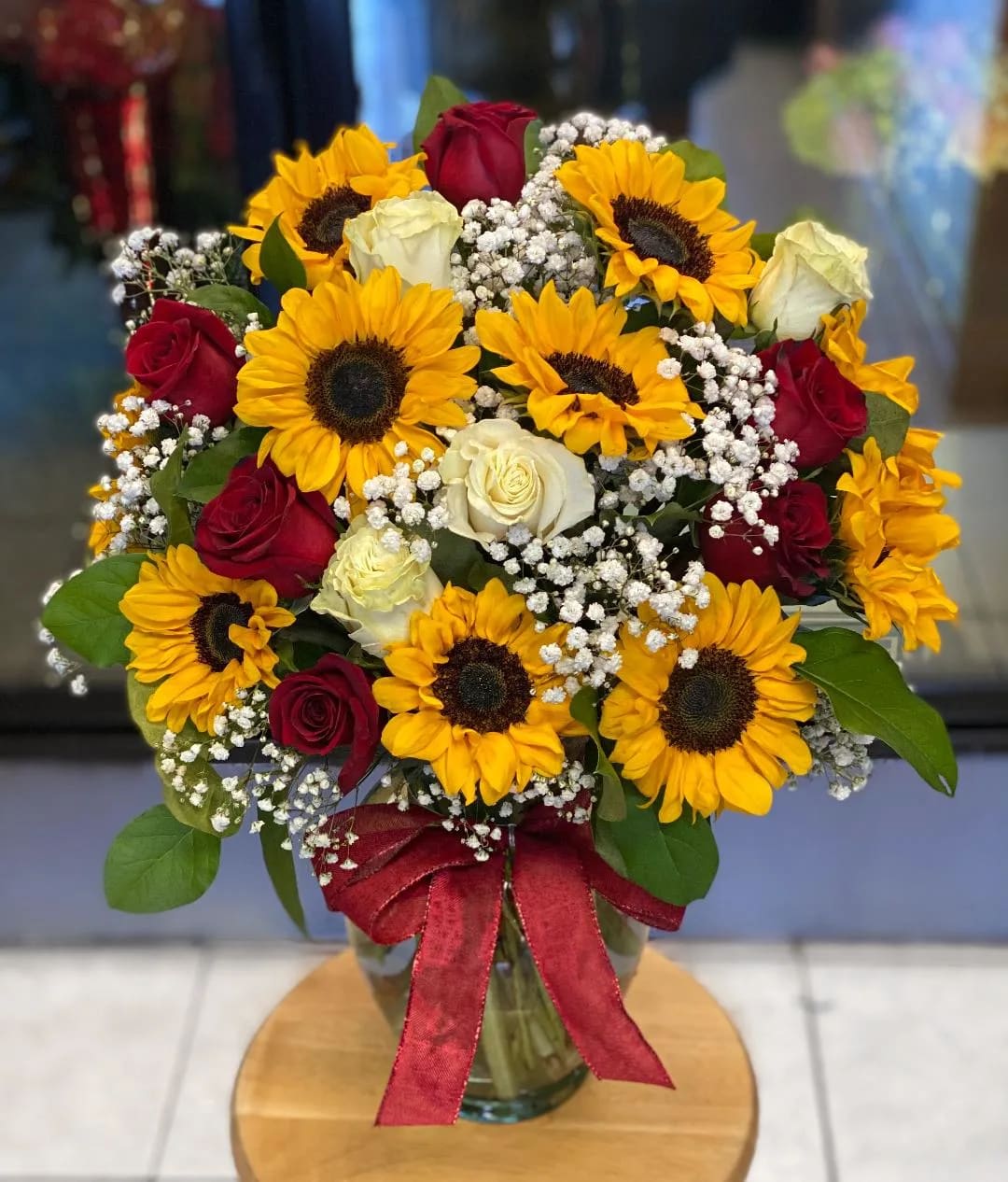 Bouquet of sunflowers and red and white roses in a glass vase with a red ribbon