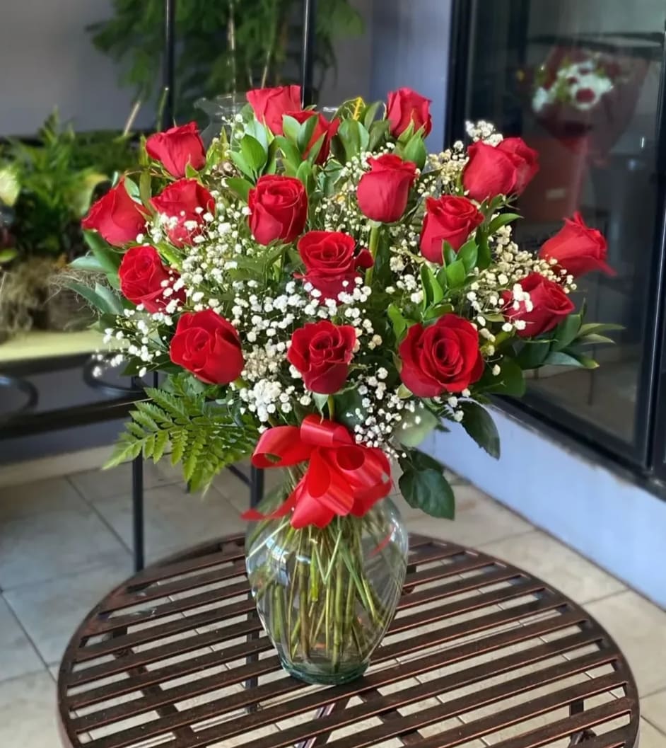 Red roses arranged in a clear glass vase with baby's breath and a red ribbon
