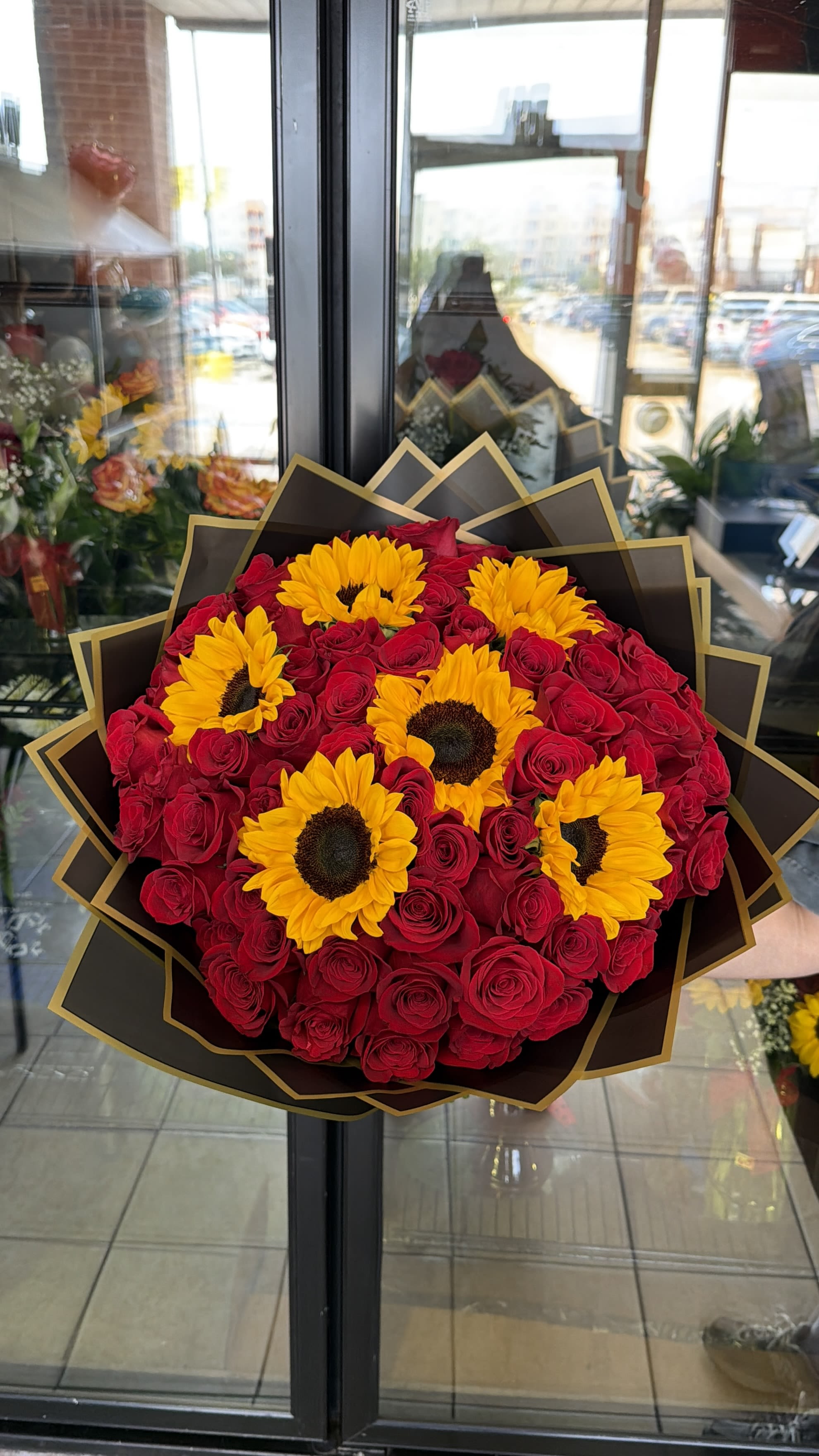 Sunrose Wrapped Bqt. - Bouquet with Red roses and sunflowers wrapped in black craft paper.  5 Dozen Red Roses and 6 Sunflowers 