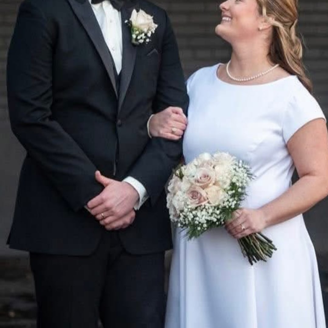 Bride holding a small white and blush bouquet beside a groom in a black suit