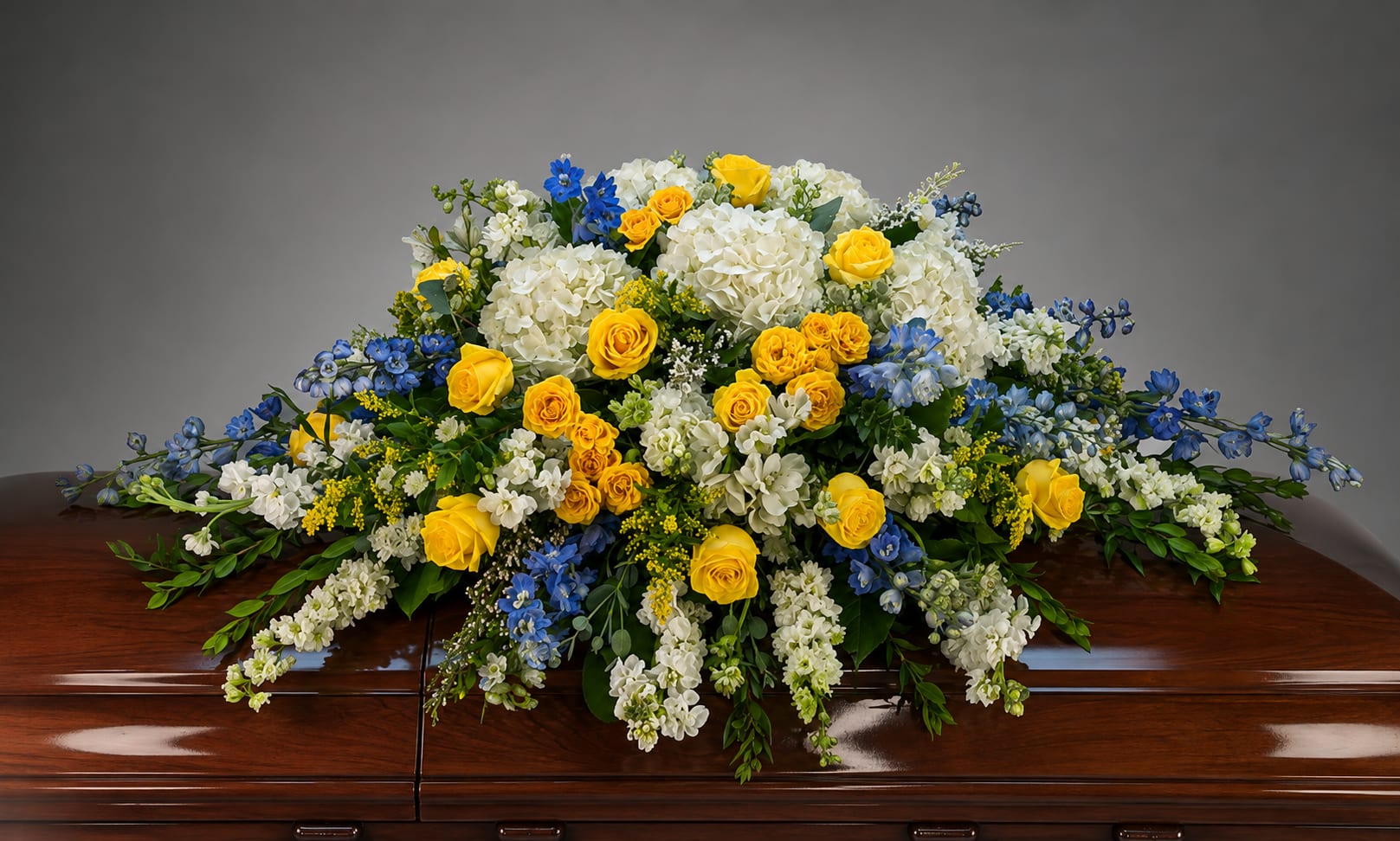 Yellow roses and white flowers arranged on a casket with blue accents