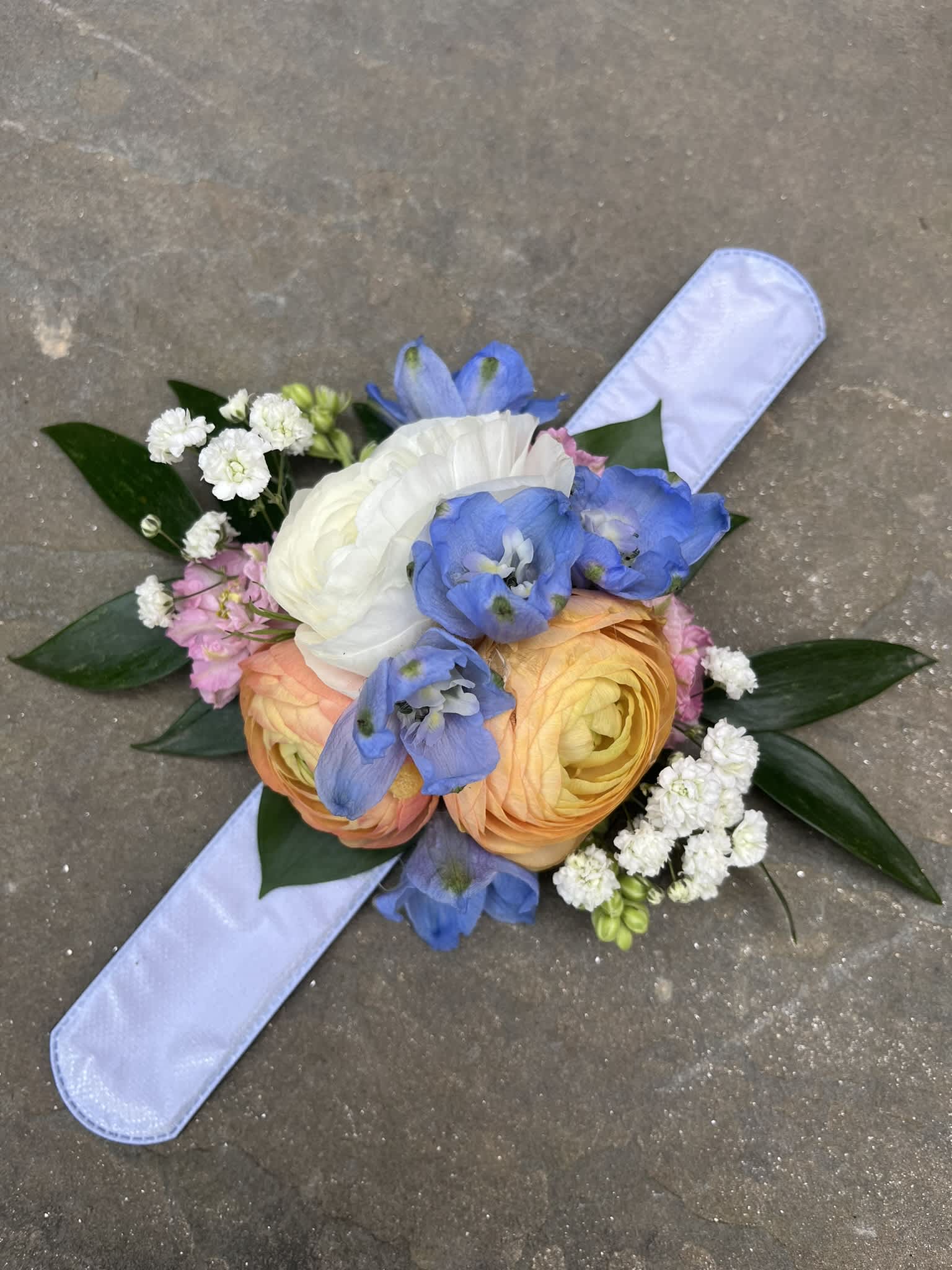 Hand-tied bouquet with blue, white, and peach flowers on a pale ribbon