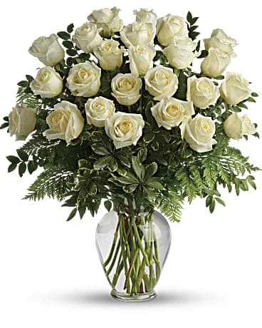 White roses arranged in a clear glass vase with greenery