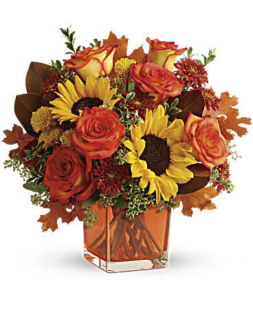 Autumn bouquet of orange roses and yellow sunflowers in a square glass vase