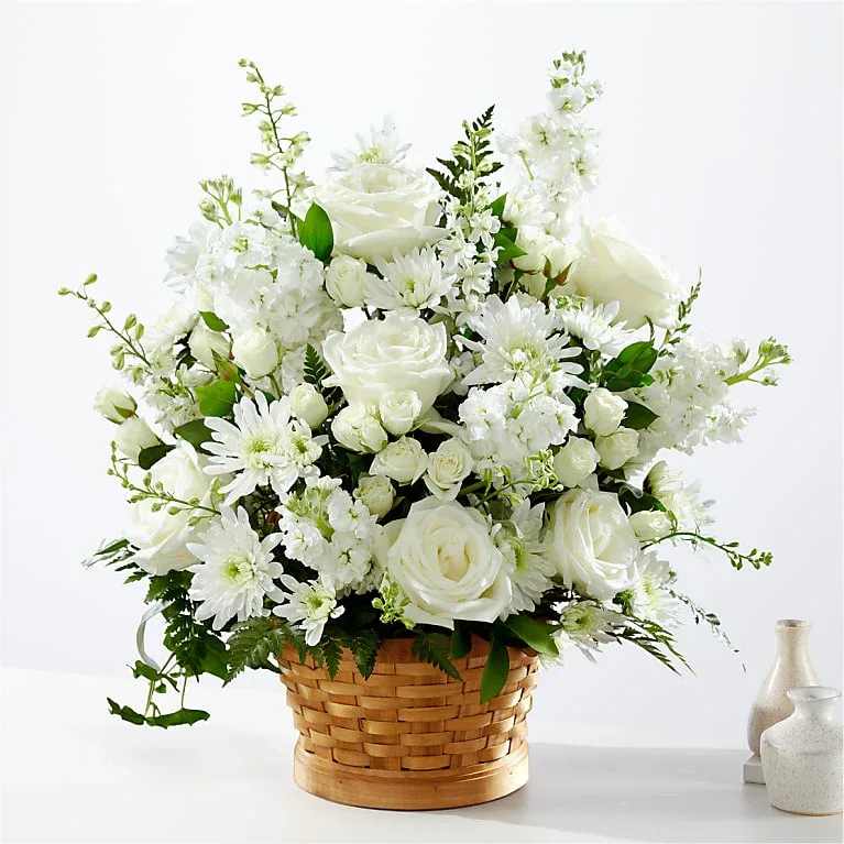 Tranquility Basket  - Let this exquisite composition of beautiful white blossoms deliver your sympathy and comfort loved ones grieving a loss. The elegance of this arrangement and its warm,  basket base makes it an appropriate addition to any wake, funeral or graveside service, or to send to the home of family or friends. Handcrafted by one of our talented florist of individually selected white roses, stock, and cushion pompons set among complementary greens for a memorable bouquet that evokes a tranquil sense of heavenly hope.   *For the freshest bouquet possible, we may replace some stems in your arrangement which could differ in color and variety.  