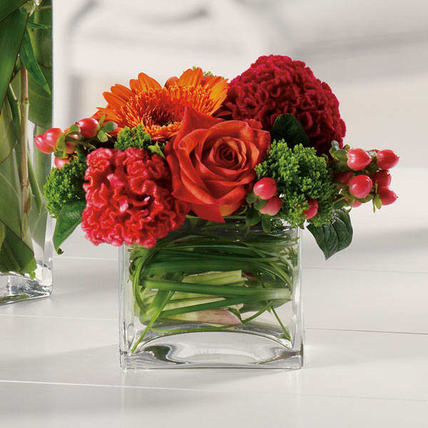 Red and orange mixed bouquet in a clear square vase