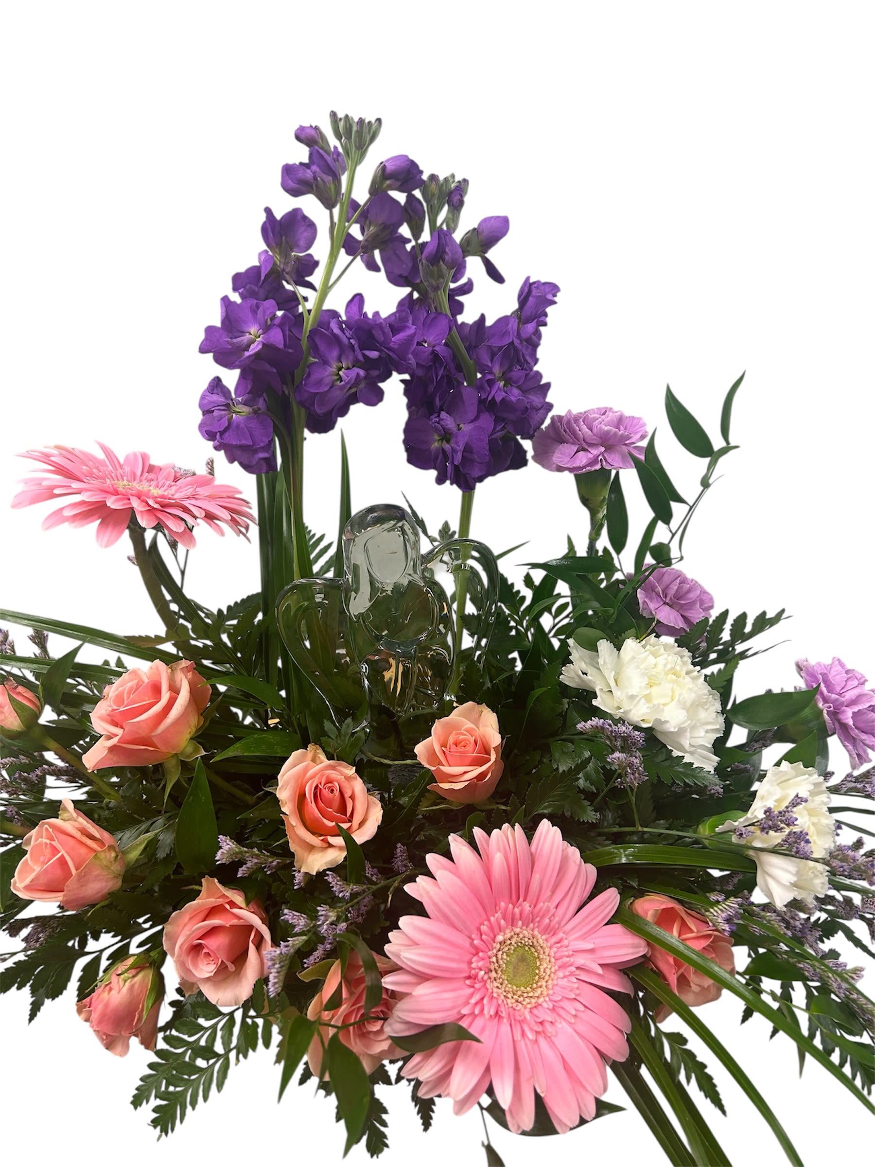 Angel Arrangement - Soft pink gerbera daisies and peach-pink roses surround a clear glass angel keepsake in this sympathy flower arrangement, creating a gently uplifting display perfect for funeral services or moments of remembrance. The combination of lavender and white carnations with tall purple stock lends a serene, comforting palette that quietly expresses care and condolence without being somber. This arrangement also suits holiday remembrances or a thoughtful gift to honor someone's memory any time of year.  