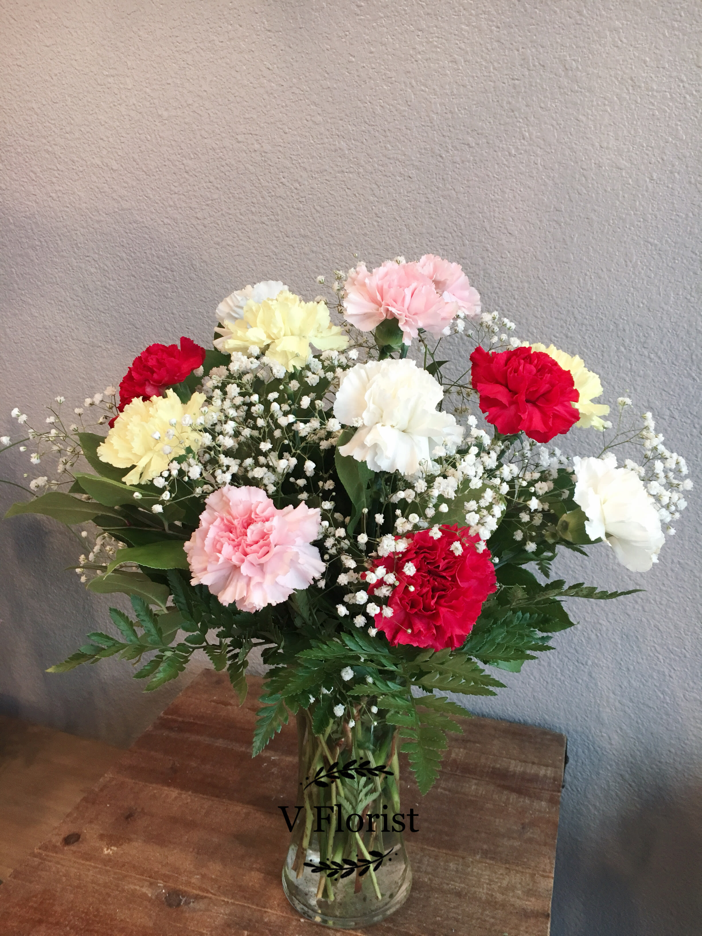 Mixed red, pink, white, and yellow carnations with baby's breath in a clear glass vase