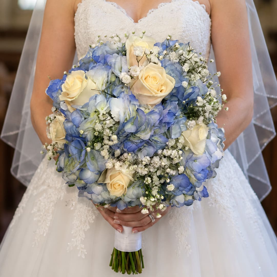 Bride holding a bouquet of blue hydrangeas and cream roses