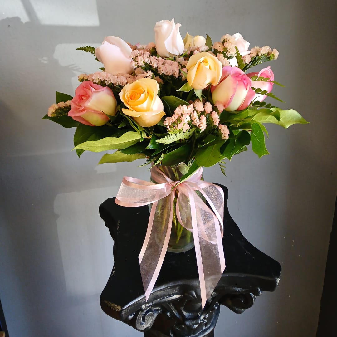 Bouquet of pastel roses in a glass vase with a pink ribbon