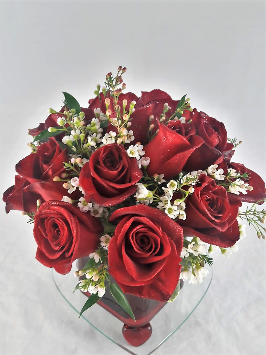 Hold Me Closer - Let someone special know how much their love means to you by sending them this truly original arrangement. A vision in red with accents was flower, this beautiful gift is a poignant way to celebrate love that endures.  Described as low and lush, this arrangement has twelve (12) fresh red roses, hand-crafted with waxflower OR status, and greens, in a cube vase.